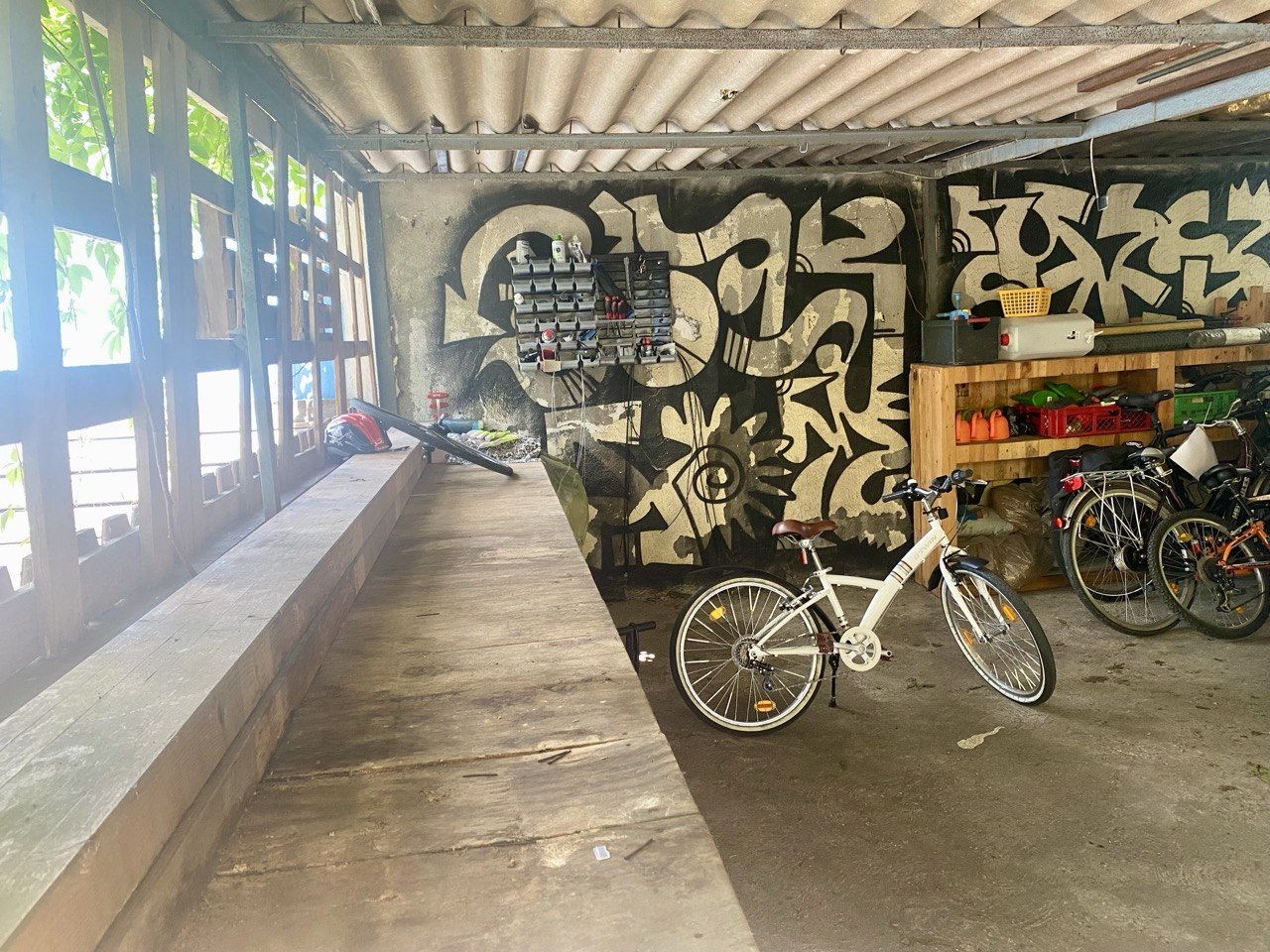 Unterstand mit Fahrrädern, Graffiti-Wandmalerei und Lagerfläche unter Wellblechdach.
