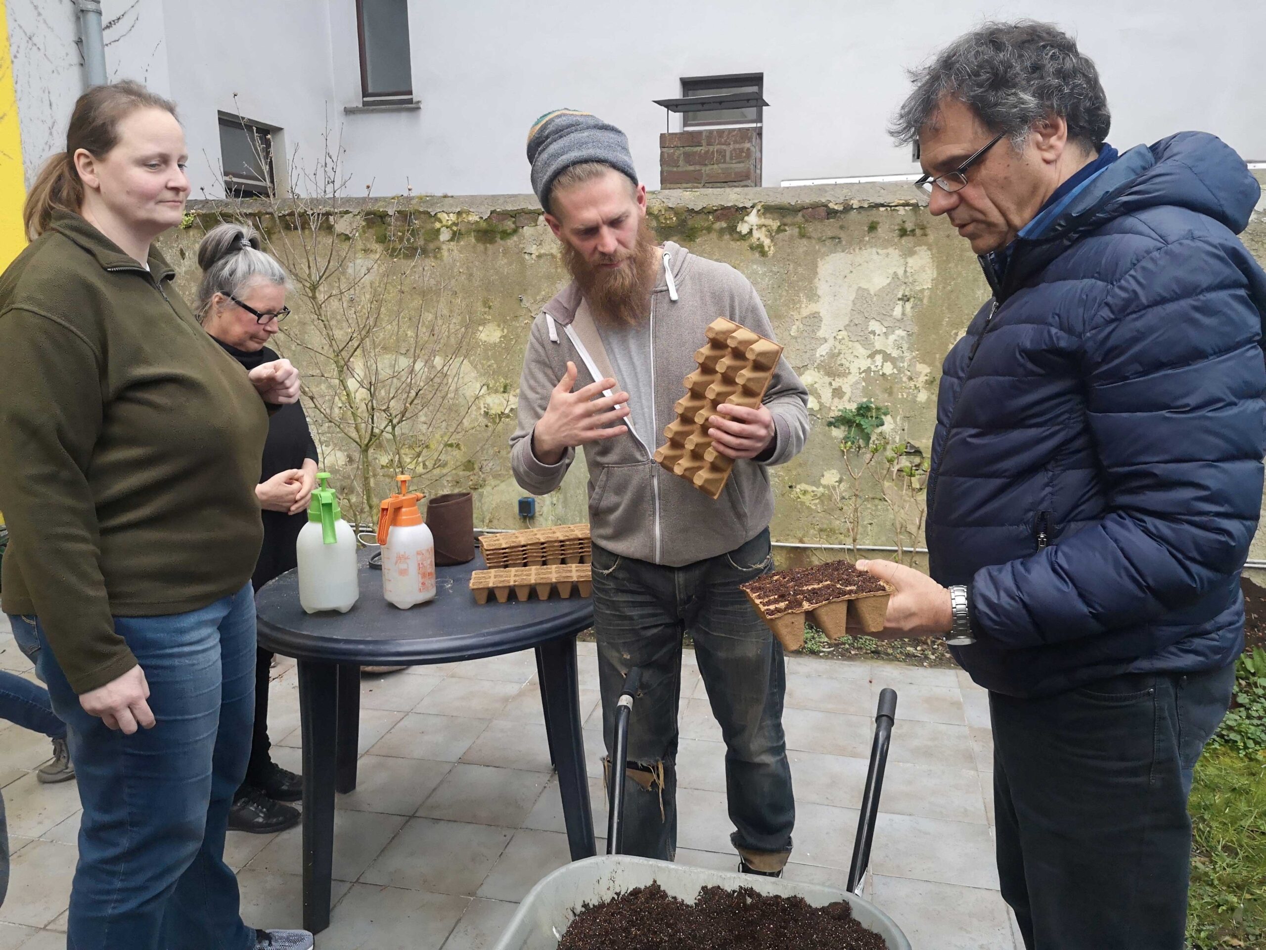 Vier Personen besprechen Anzuchtboxen bei einem Workshop zu urbaner Gartenarbeit auf einer Terrasse.