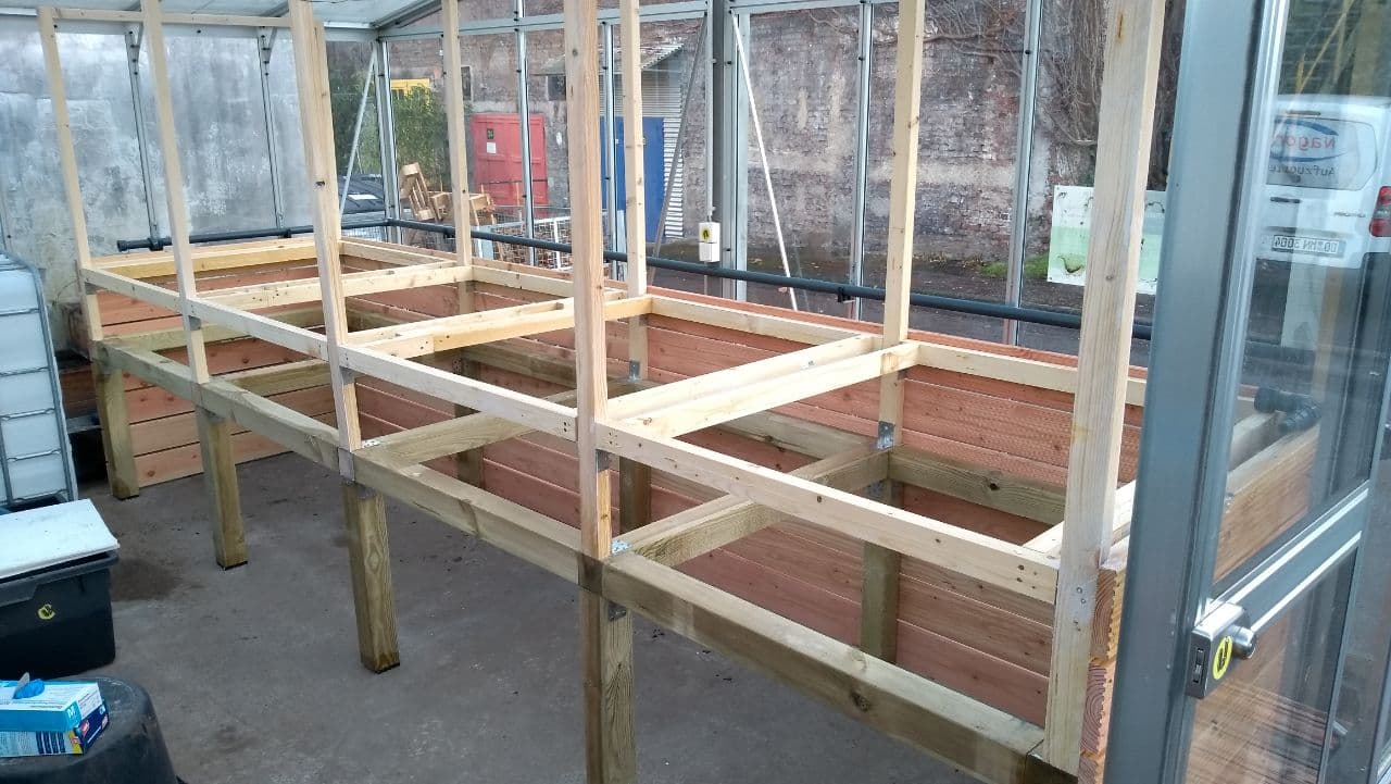 Holzkonstruktion mit Hochbeeten in Gewächshaus während Aufbau oder Renovierung.
