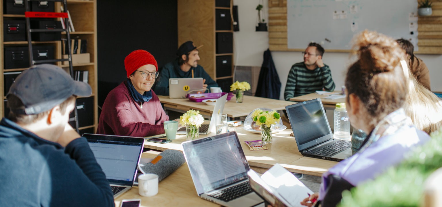 Mehrere Personen sitzen an einem Tisch mit Laptops in einem modernen Büroraum zusammen.