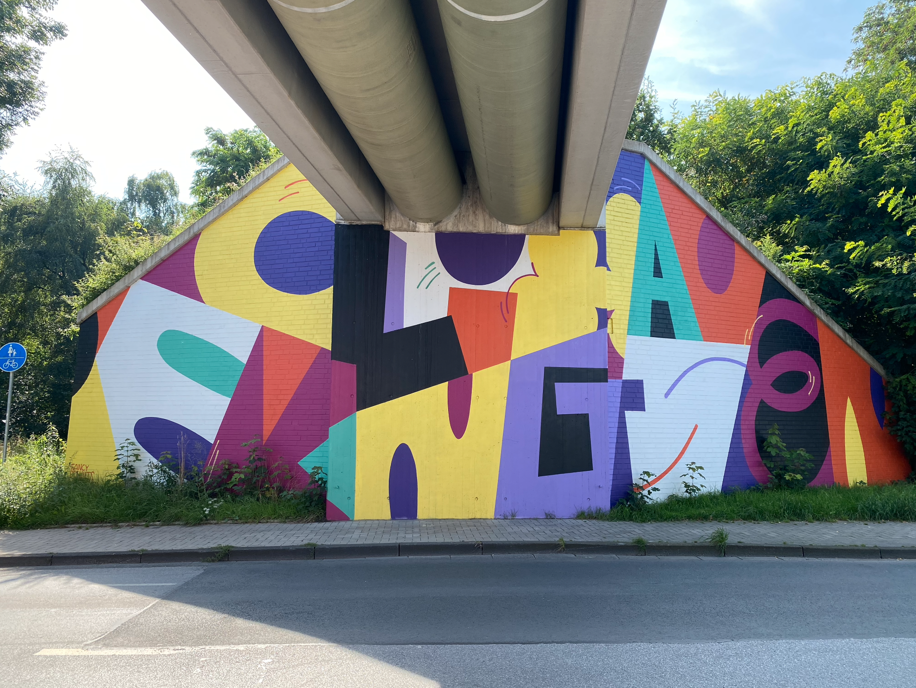 Bunte abstrakte Wandmalerei unter einer Brücke mit geometrischen Formen und Farbflächen.