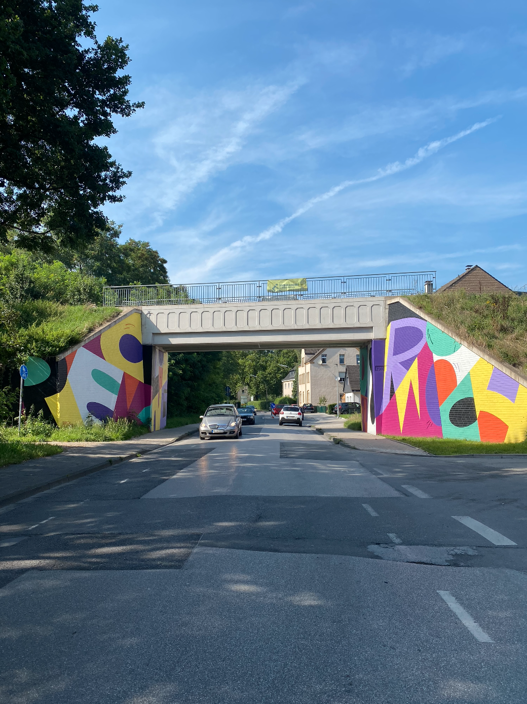 Unterführung mit buntem Graffiti-Kunstwerk, Straße mit Autos und Bäumen.