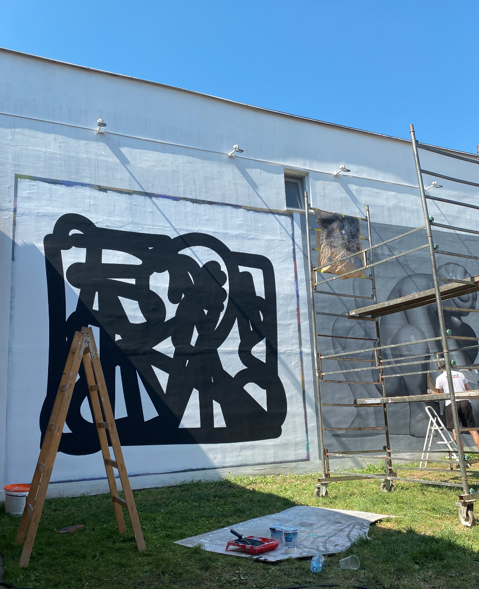 Künstler bemalt eine weiße Hauswand mit großformatigem schwarzem abstraktem Muster unter freiem Himmel.