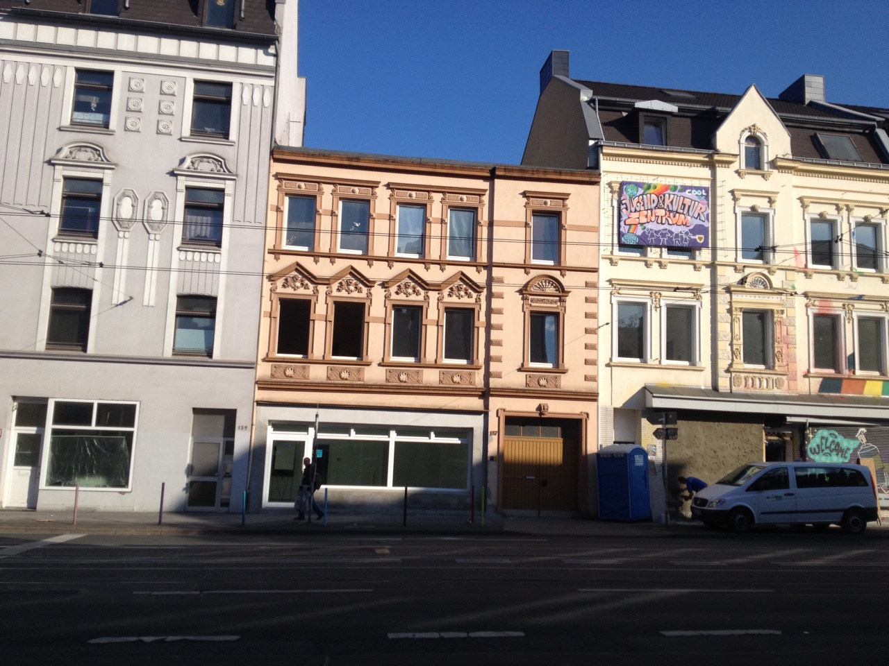 Straßenfront mit vier mehrstöckigen Wohngebäuden unterschiedlicher Baustile und Fassadenfarben.