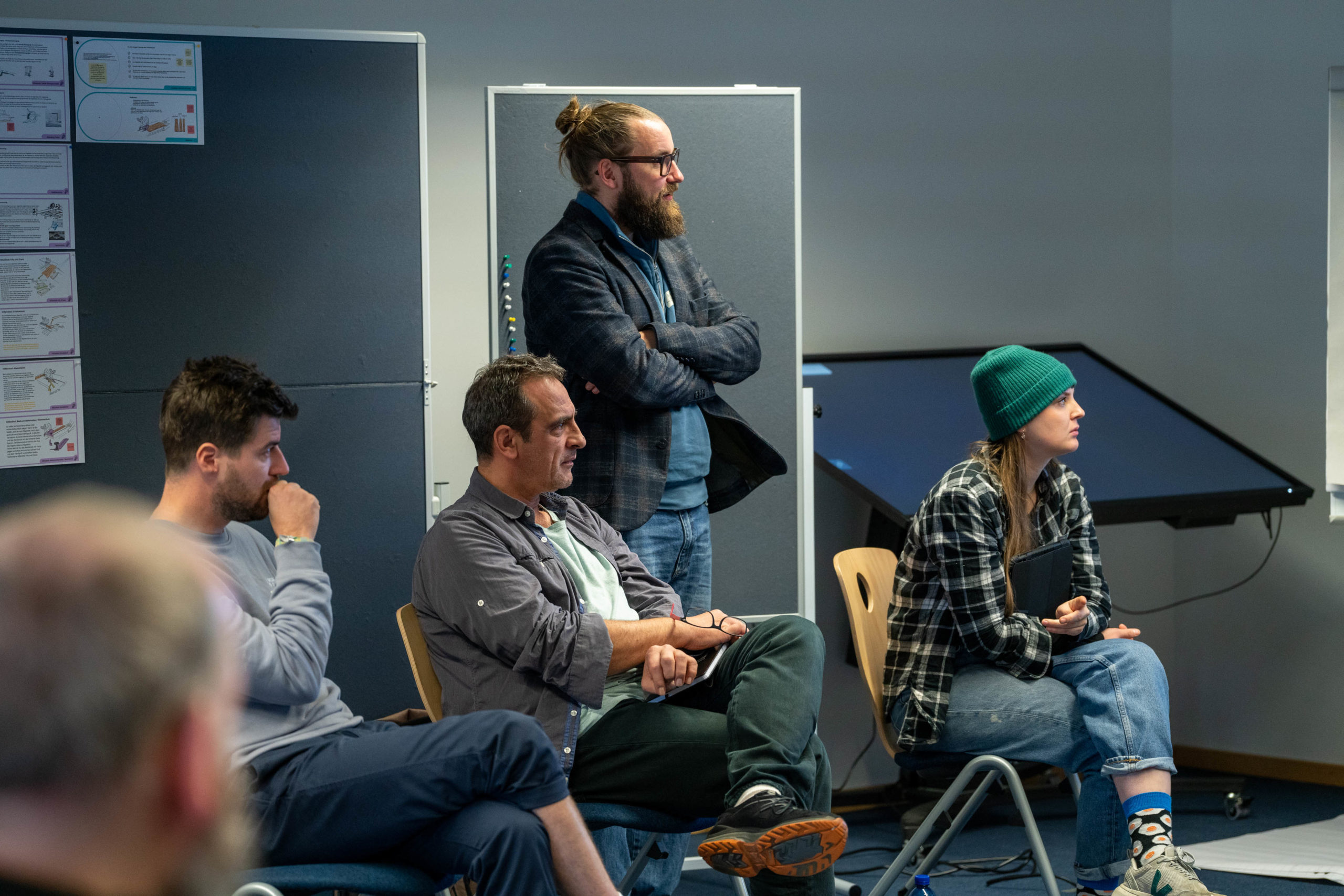 Mehrere Personen sitzen und stehen in einem Seminarraum während einer Diskussionsveranstaltung.