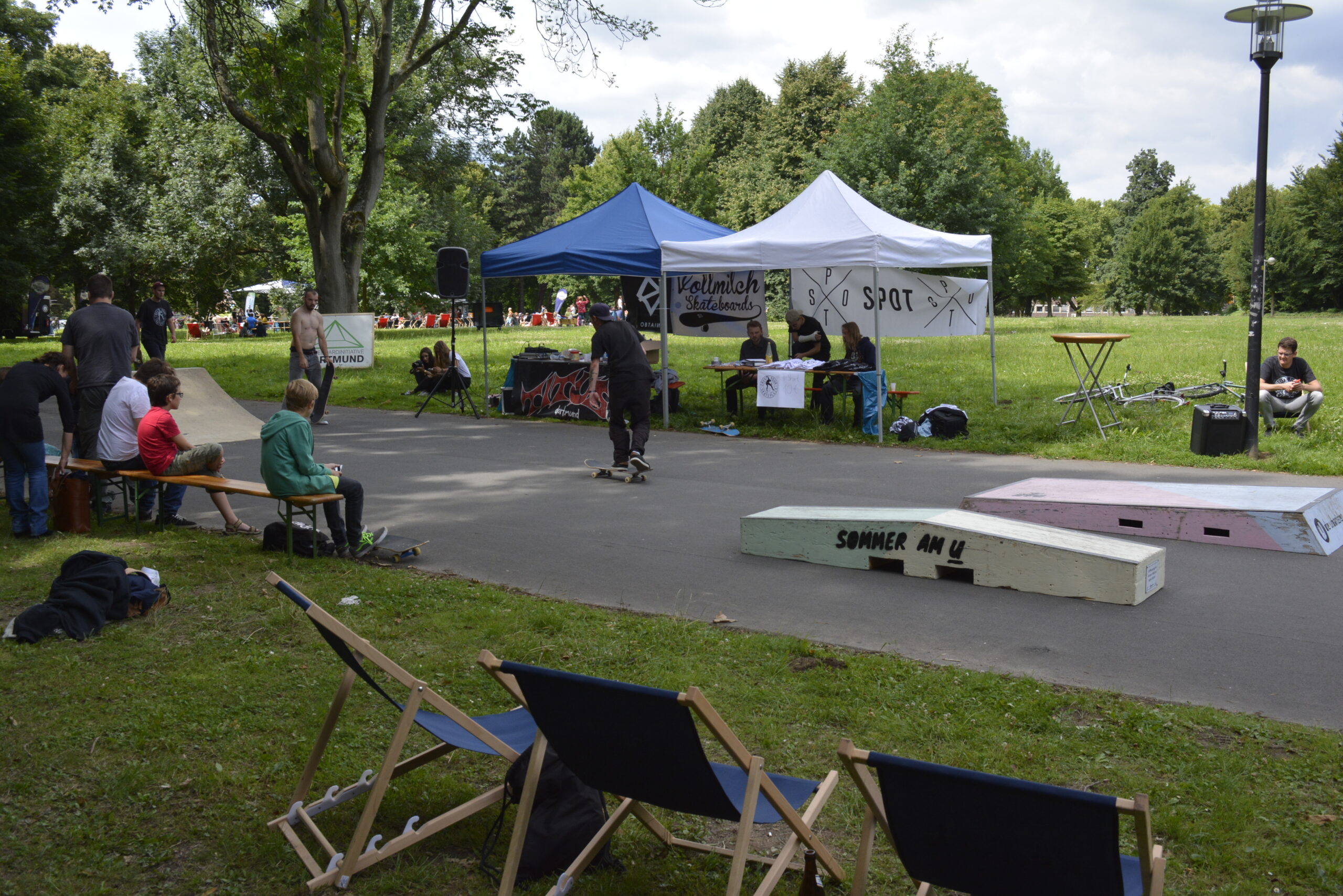 Skatepark-Veranstaltung in einem Park mit Zelten, Zuschauern und Sitzmöglichkeiten.