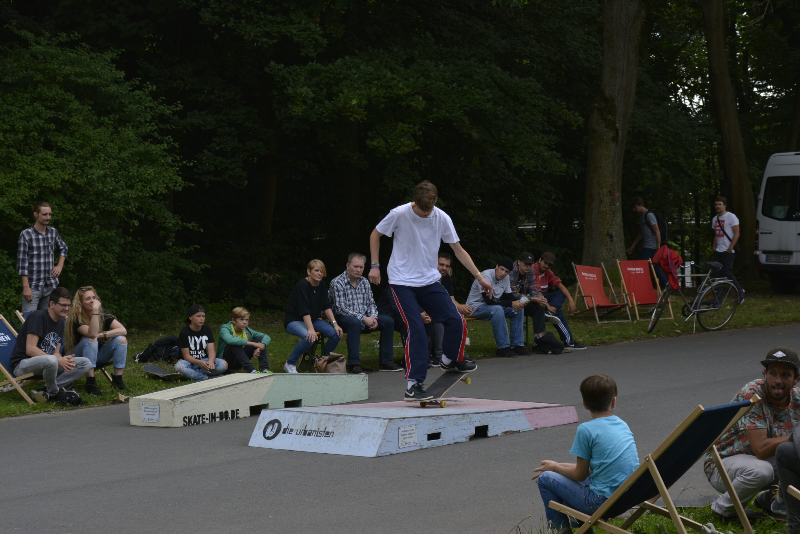 Skateboarder führt Trick auf Rampe vor Publikum in Park auf.