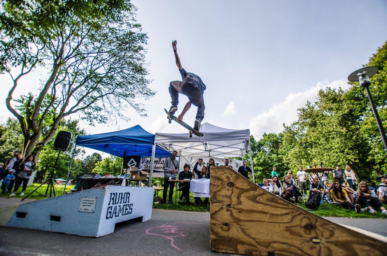 Skateboarder springt über Rampe bei Blindgames-Event vor Publikum im Park.