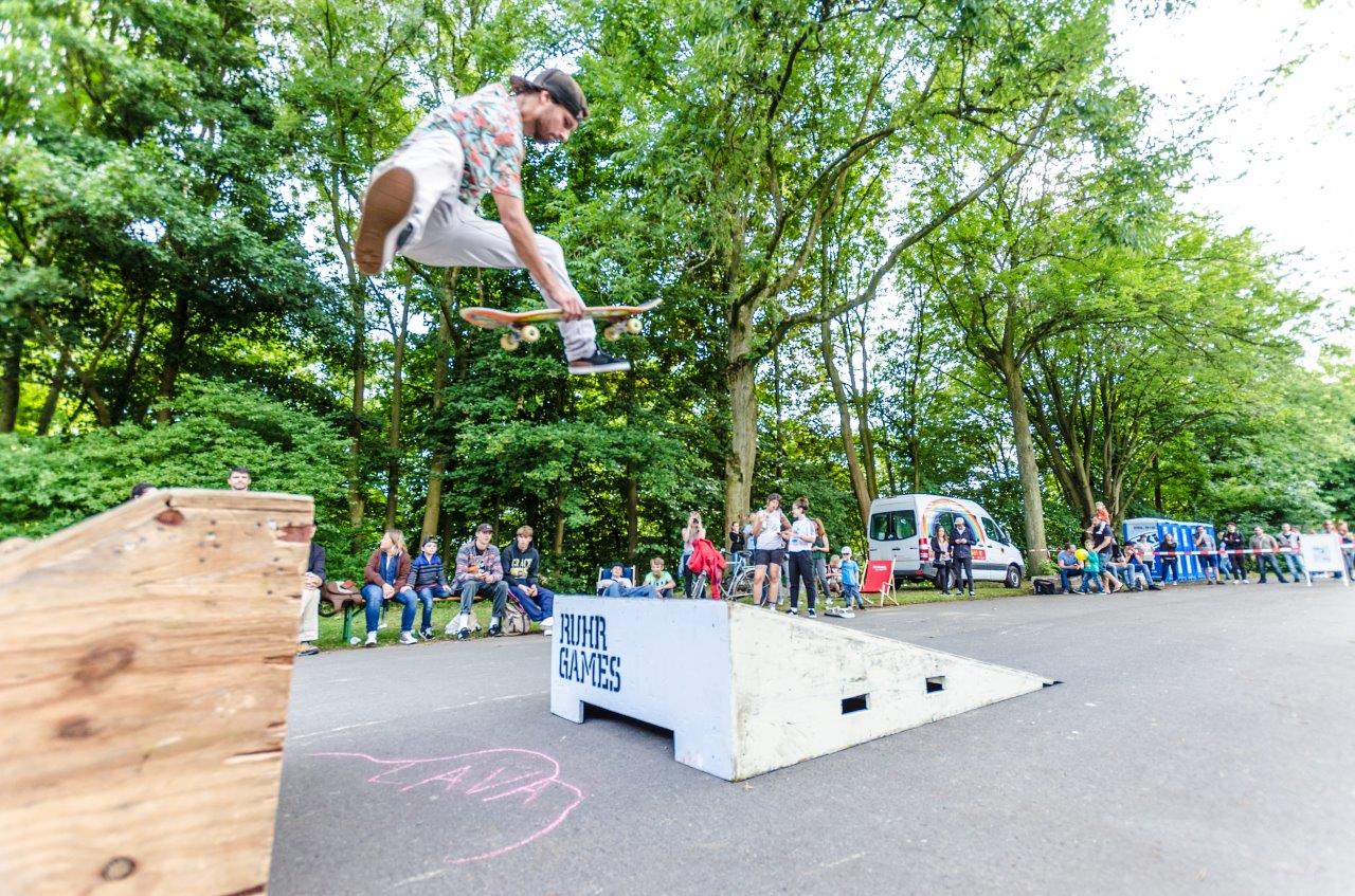 Skateboarder springt über Hindernis bei Ruhr Games Event vor Zuschauern im Park.