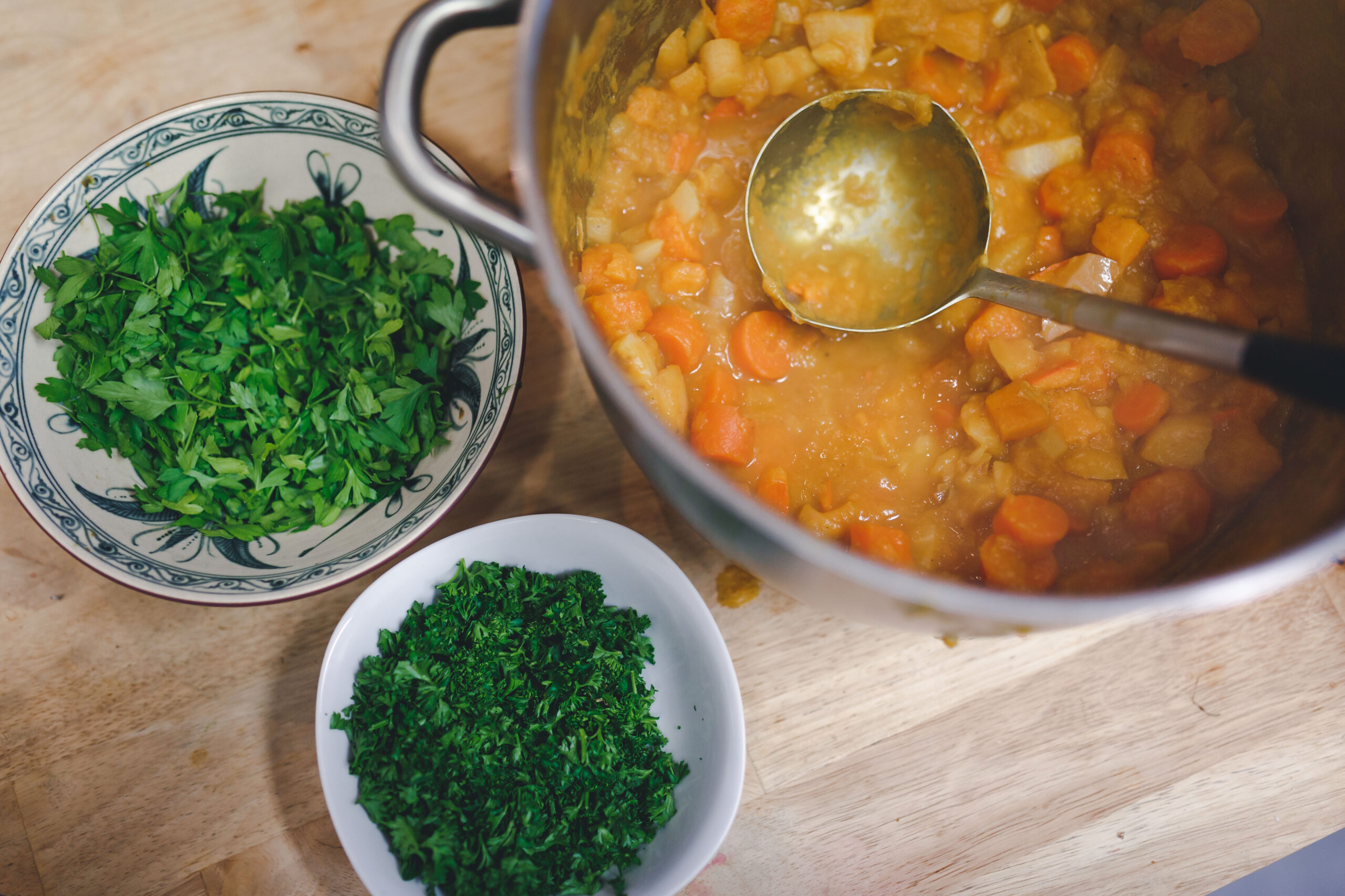 Kochszene mit Topf Gemüsesuppe, Ladle und frischer Petersilie in zwei Schüsseln.