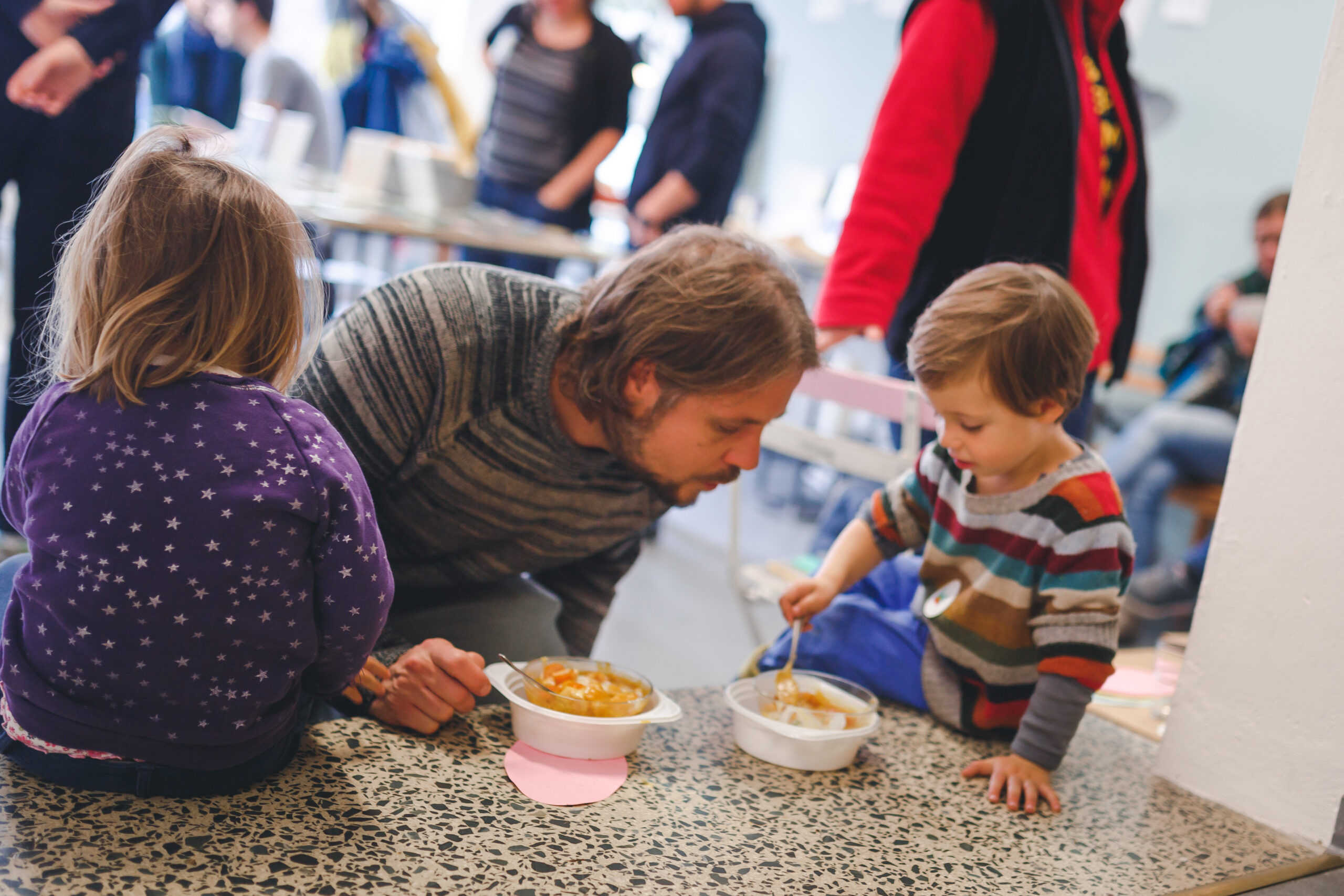 Erwachsene und Kinder essen gemeinsam an einem Tisch während einer Gemeinschaftsveranstaltung.