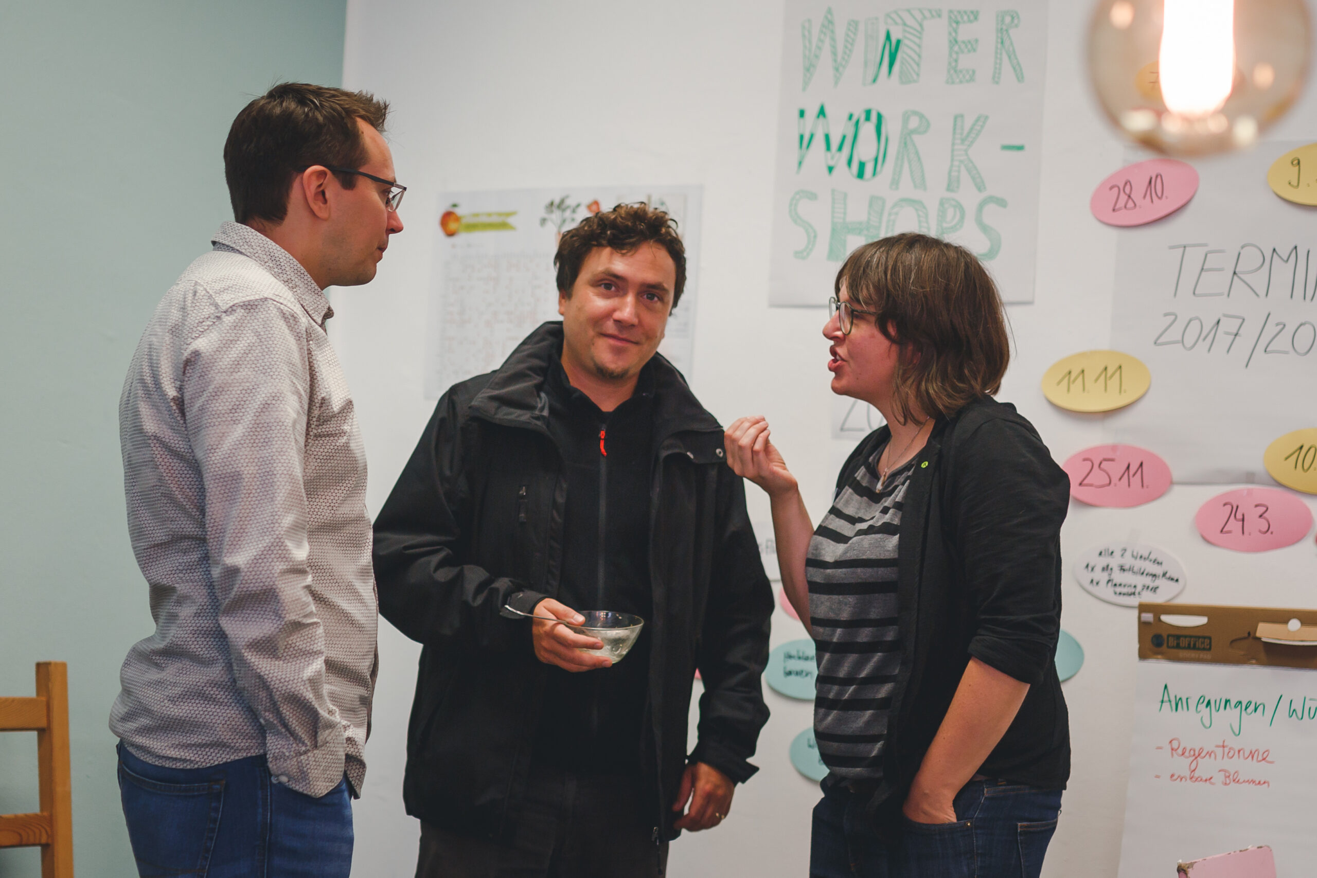 Drei Personen diskutieren vor einer Pinnwand mit Notizen zu Stadtentwicklung und Workshops.