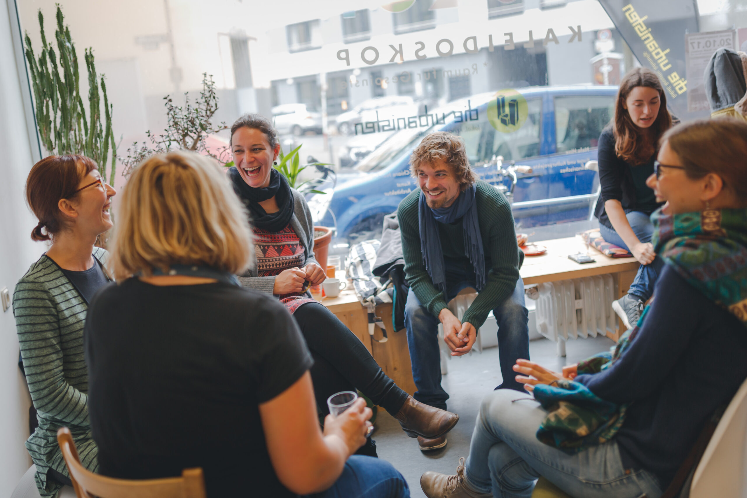 Eine Gruppe von etwa acht Personen sitzt in einem Kreis und diskutiert lebhaft in einem hellen Büroraum.