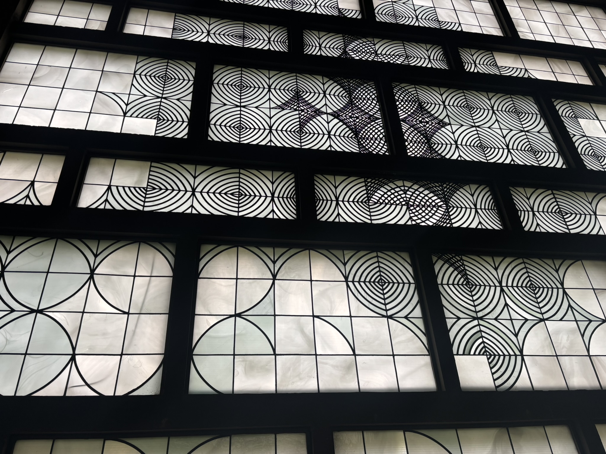 Fensterfront mit schwarzem Rahmen und Glasflächen, teilweise mit geometrischen Mustern verziert.
