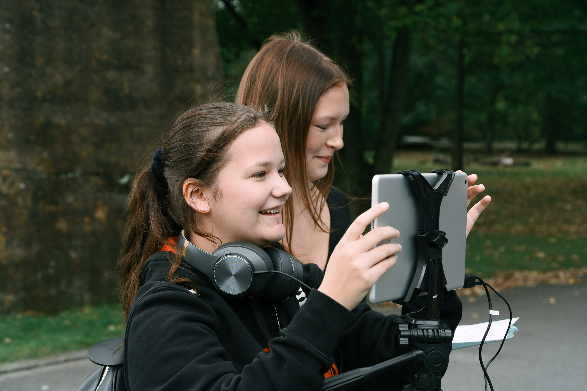 Zwei Mädchen filmen outdoor mit Tablet und Stativ in einem Park.