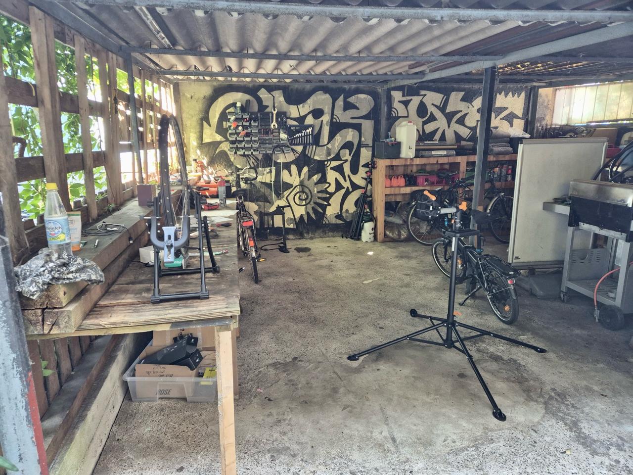 Fahrradwerkstatt in einer Industriehalle mit Graffiti an den Wänden und Reparaturständen.