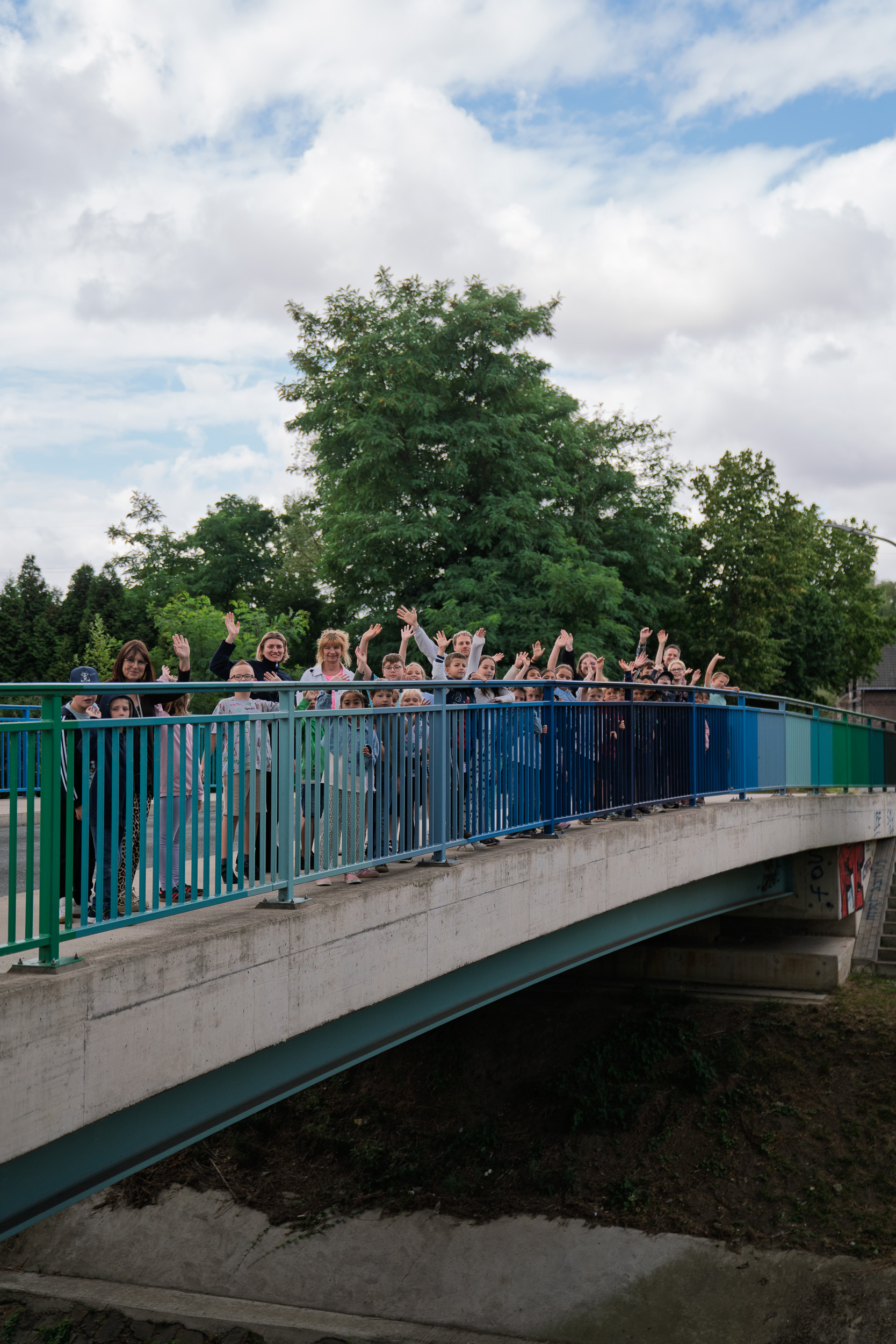 Gruppe von Menschen auf einer grünen Brücke über einen Bach, winkend.