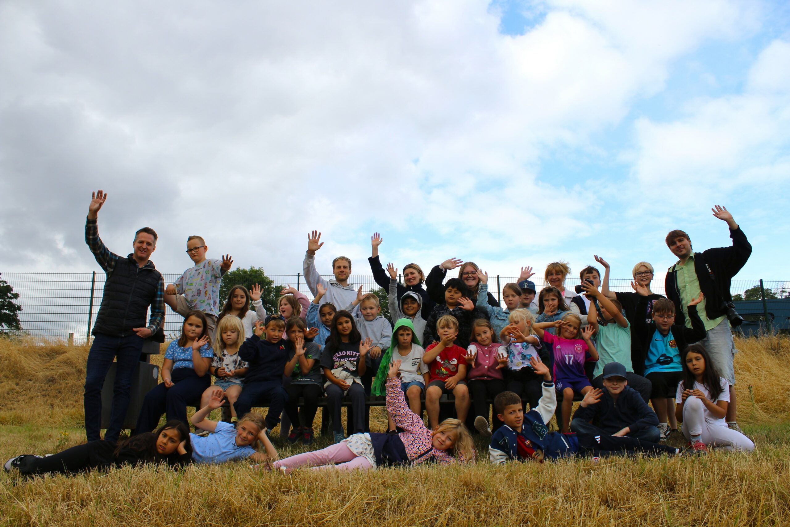 Große Gruppe von Kindern und Erwachsenen posiert fröhlich auf einer Wiese.