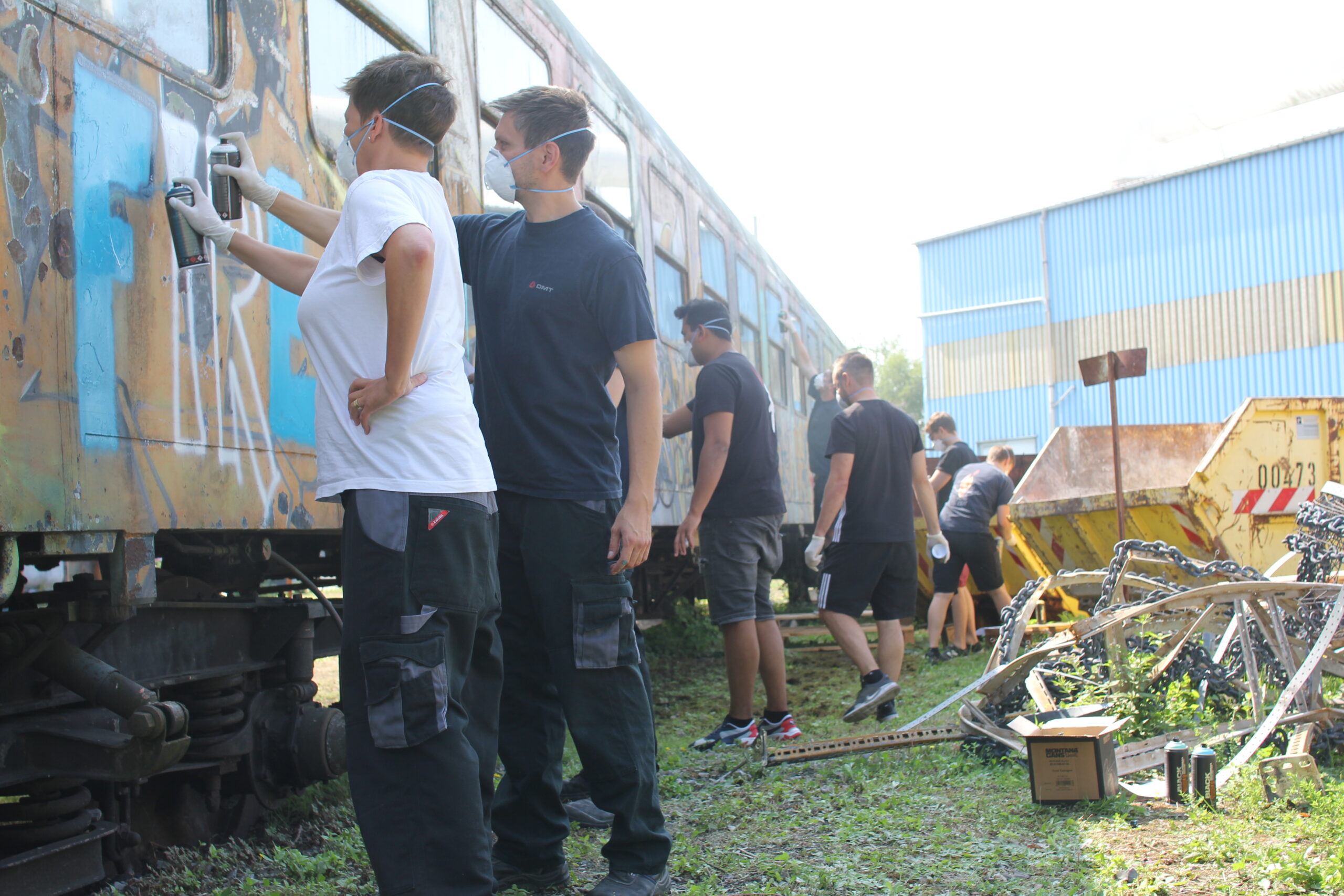 Gruppe von Menschen besichtigt einen ausrangierten Eisenbahnwagon auf einem Gelände.