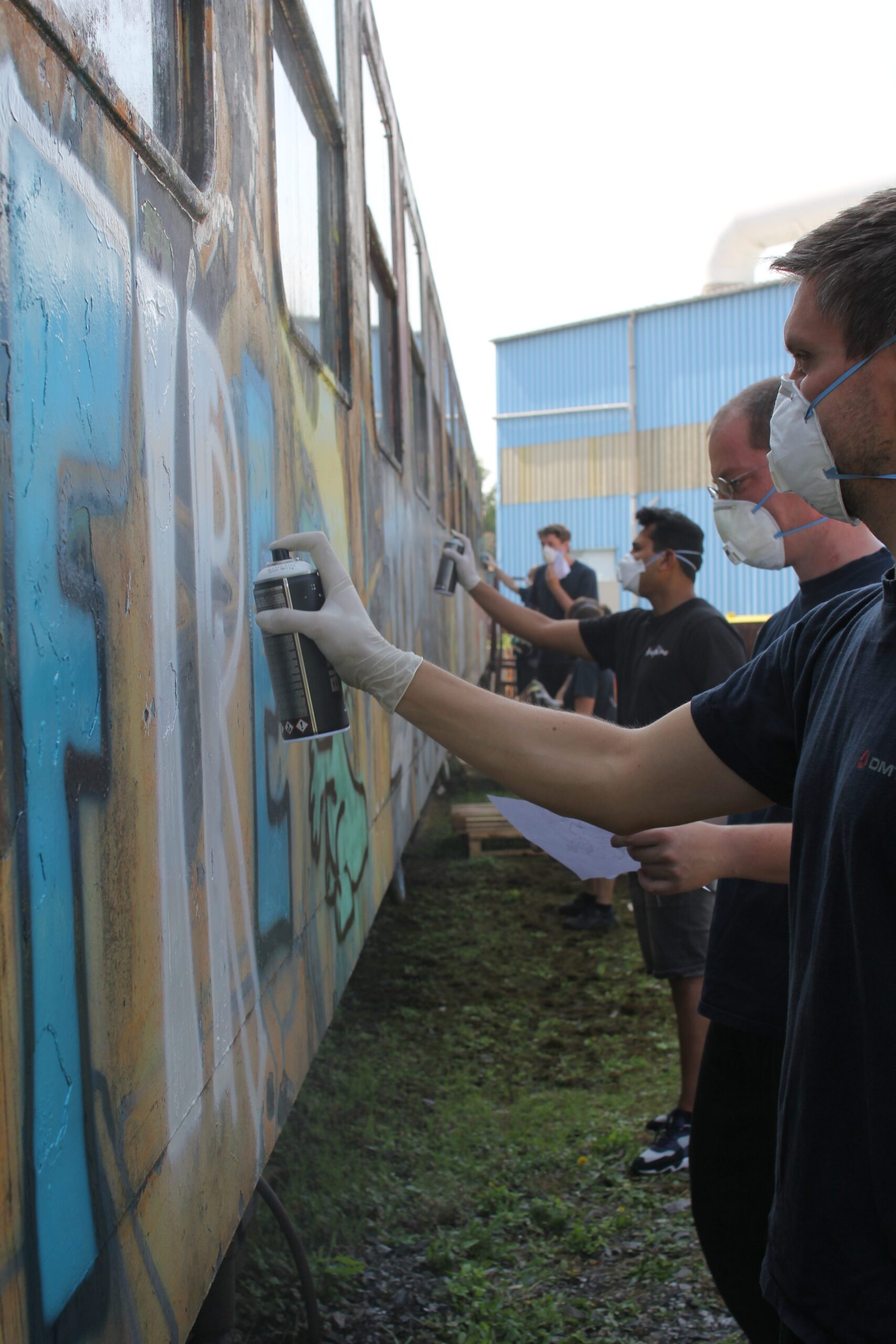 Personen mit Schutzmasken dokumentieren Graffiti an einer Metallwand mit Messgeräten.