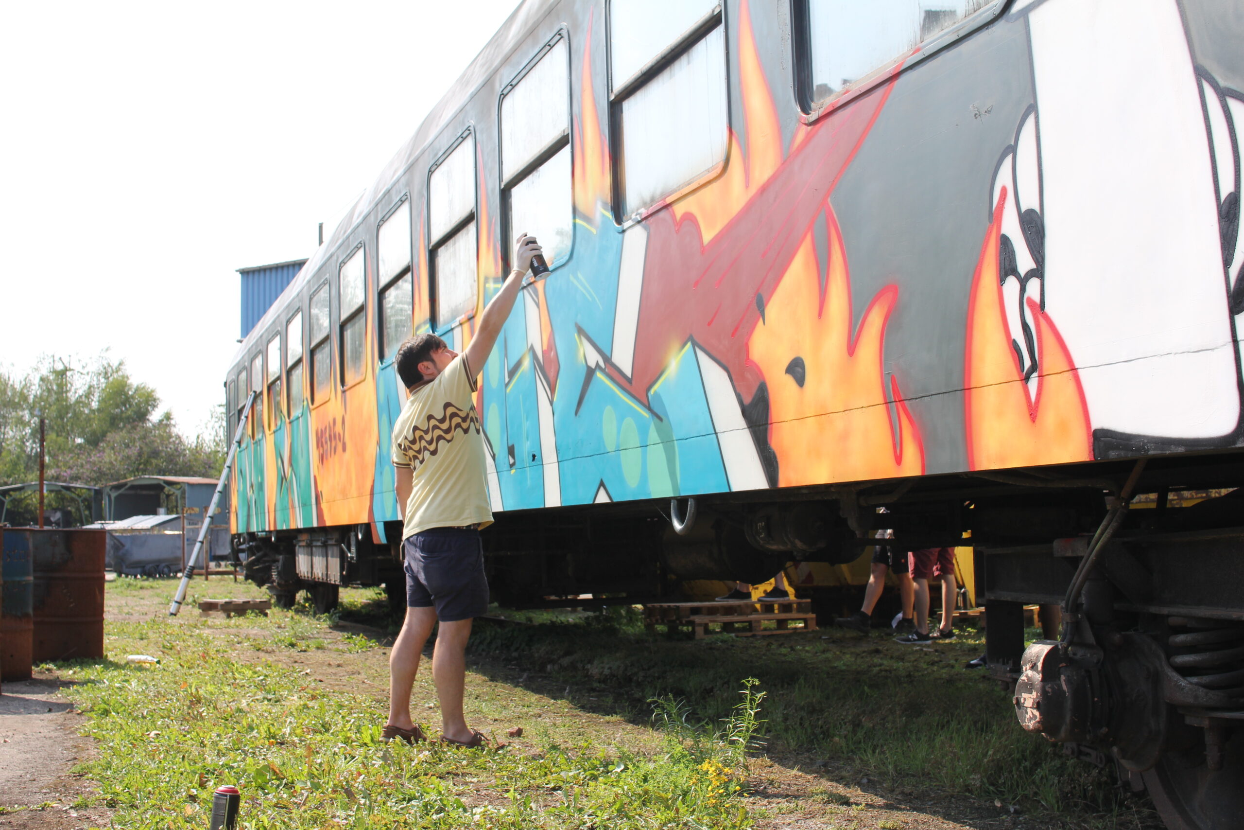 Ein Mann bemalt mit Spraydose die Seitenwand eines Zugwagons mit farbigem Graffiti.