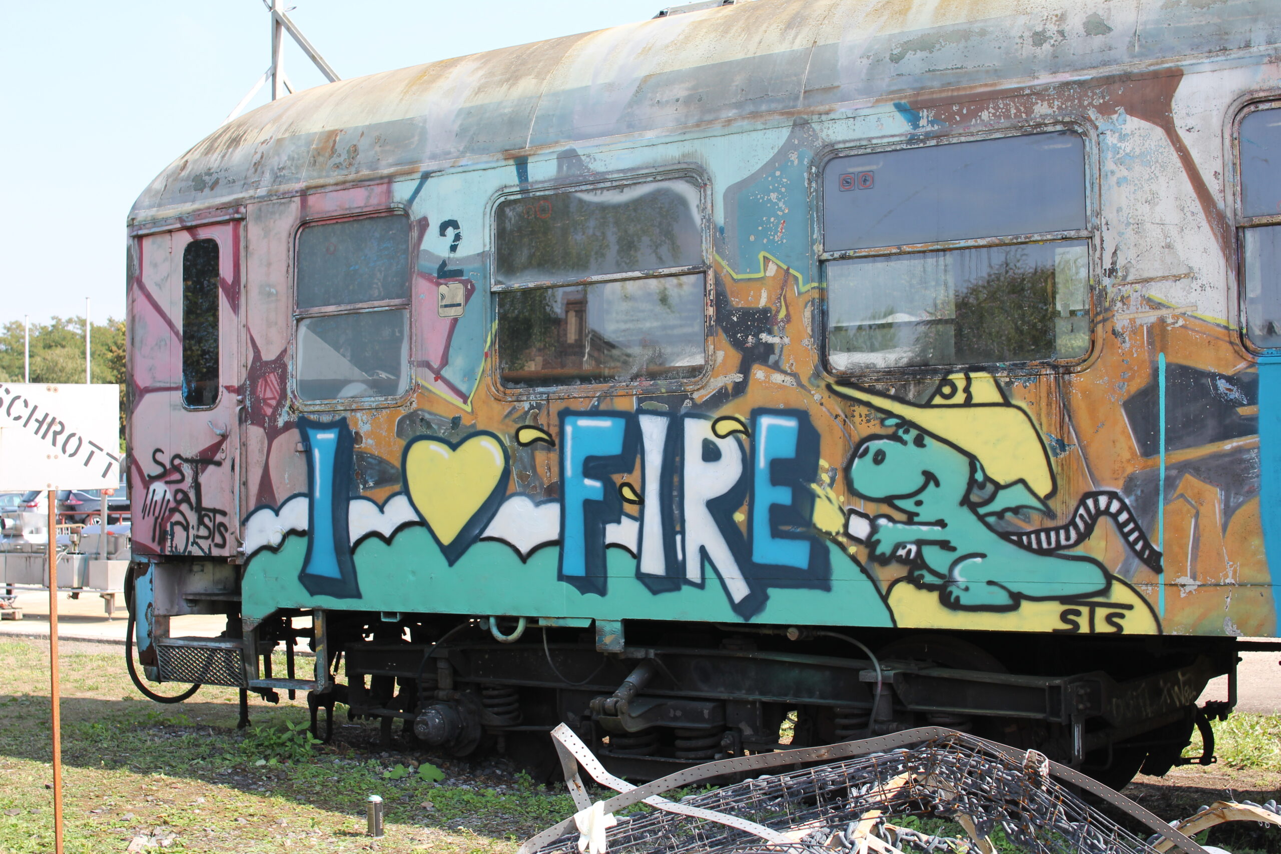 Ein bemalter Eisenbahnwaggon mit buntem Graffiti steht auf einem Gelände.