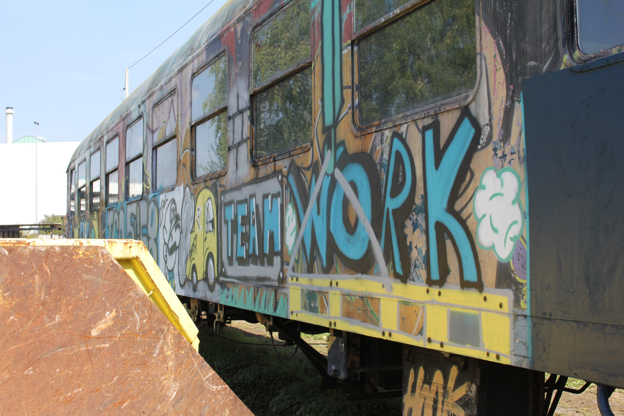 Alter Eisenbahnwagen mit bunten Graffiti-Kunstwerken in einer Industriebrache steht.