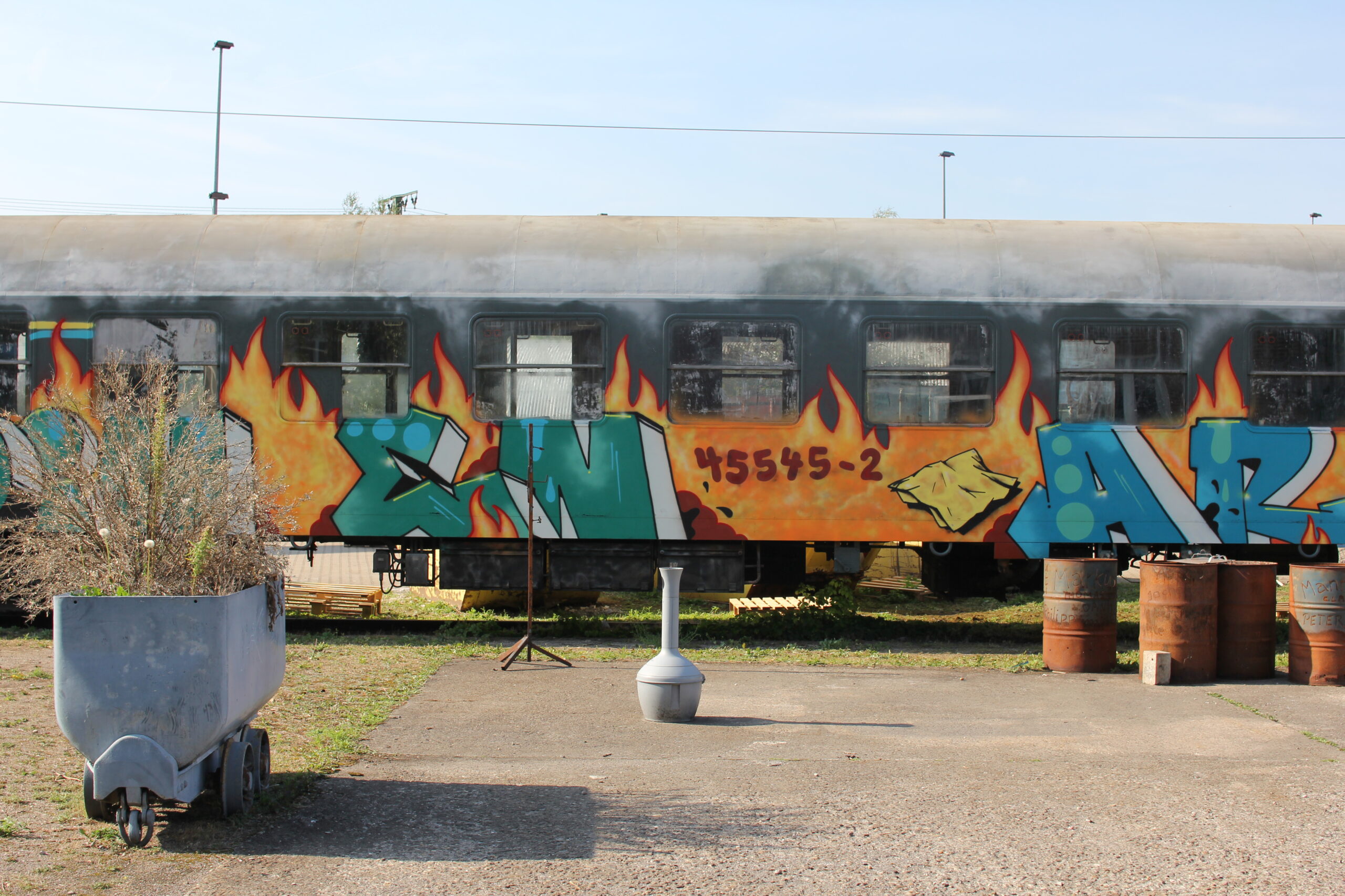 Ein bemalter Güterwagen mit Graffiti-Kunstwerk steht auf Gleisen neben Metallcontainern.