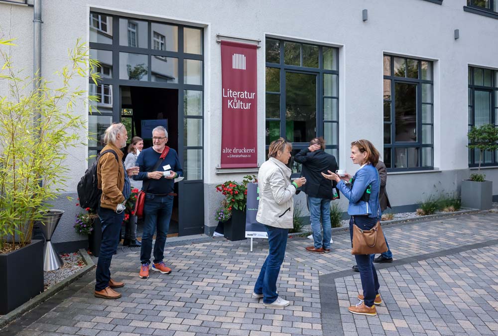 Mehrere Personen stehen auf einem gepflasterten Platz vor einem Gebäude mit Literatur-Kultur-Banner.