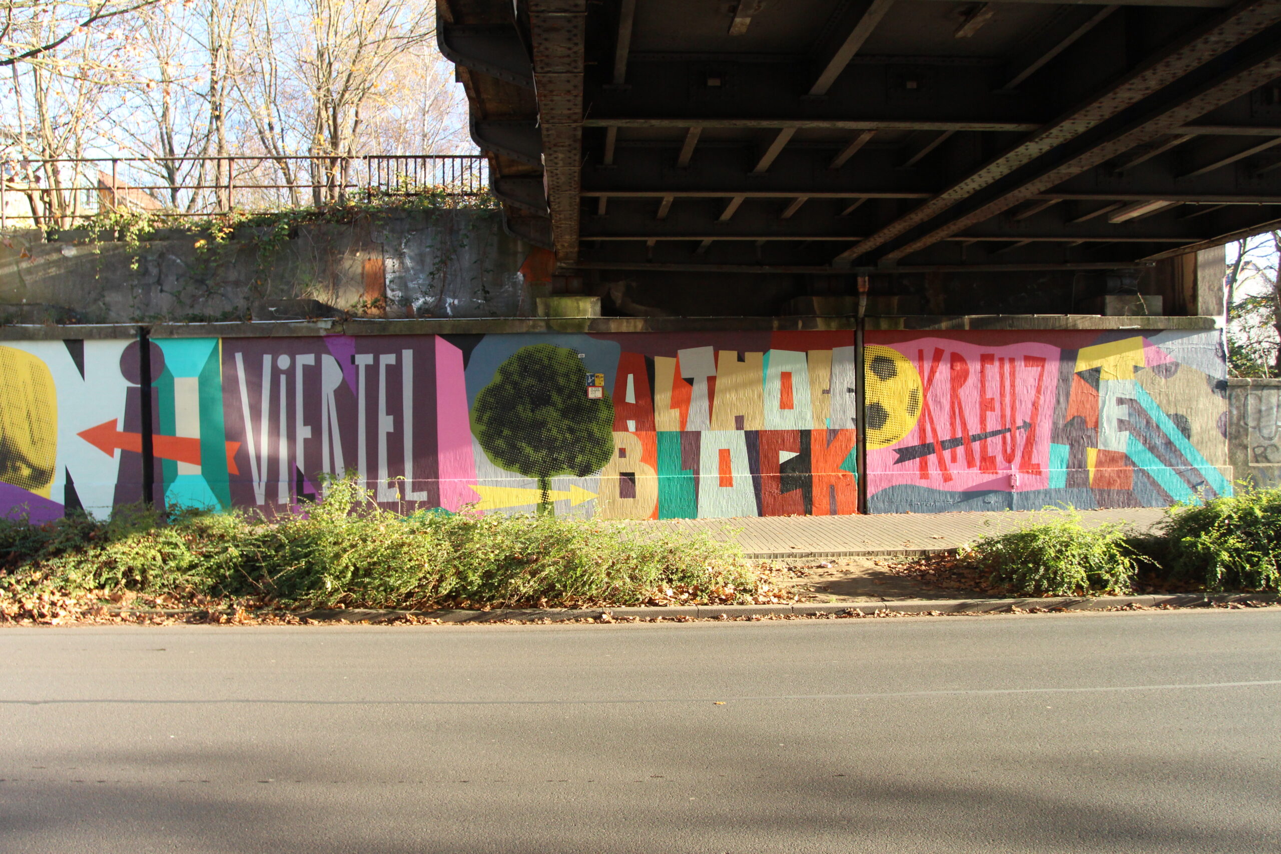 Buntes Wandgemälde unter einer Brücke mit abstrakten Formen und Schriftzügen in verschiedenen Farben.