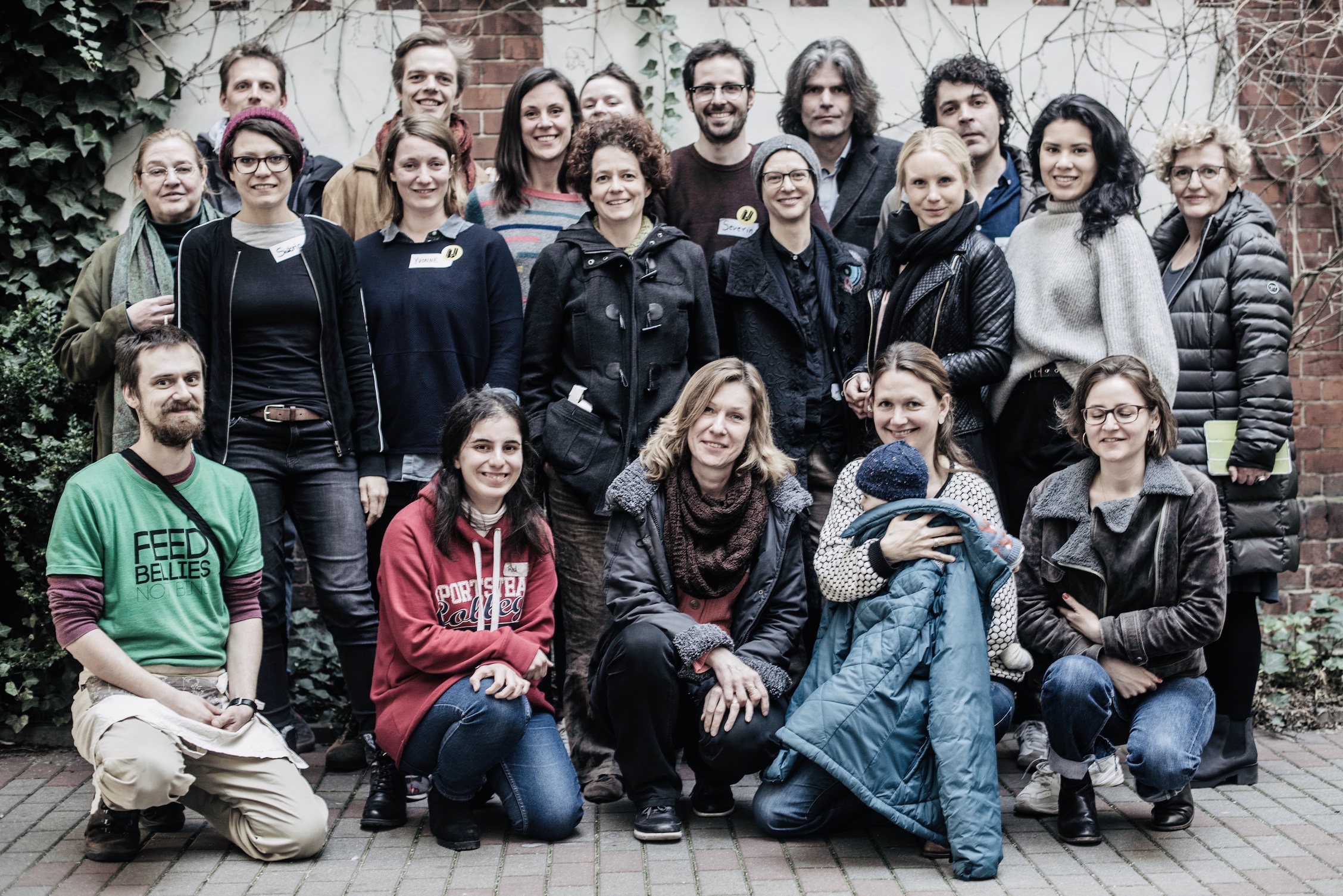 Gruppenfoto von etwa 25 Personen verschiedenen Alters vor einer Backsteinmauer mit Efeu.