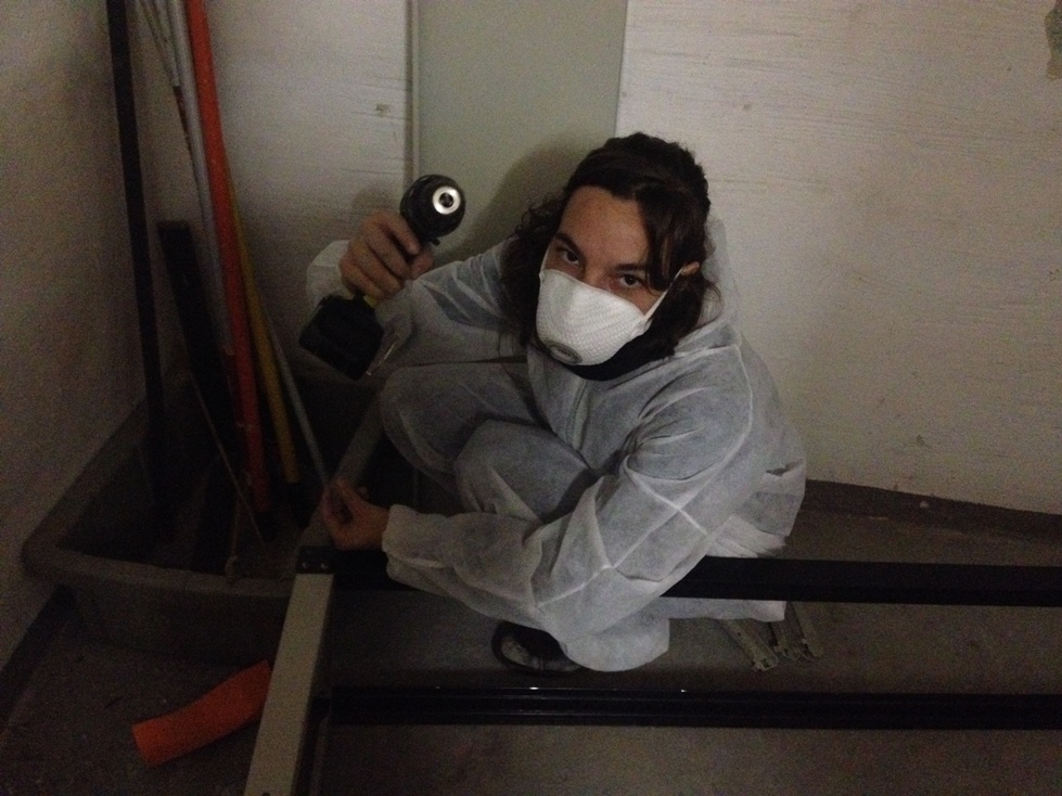 Person mit Maske hält Bohrmaschine in Werkstatt oder Baustelle.