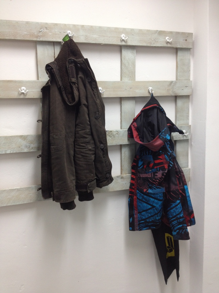An einer Holzpalette hängen eine schwarze Jacke und eine bunte Kinderjacke mit Haken.