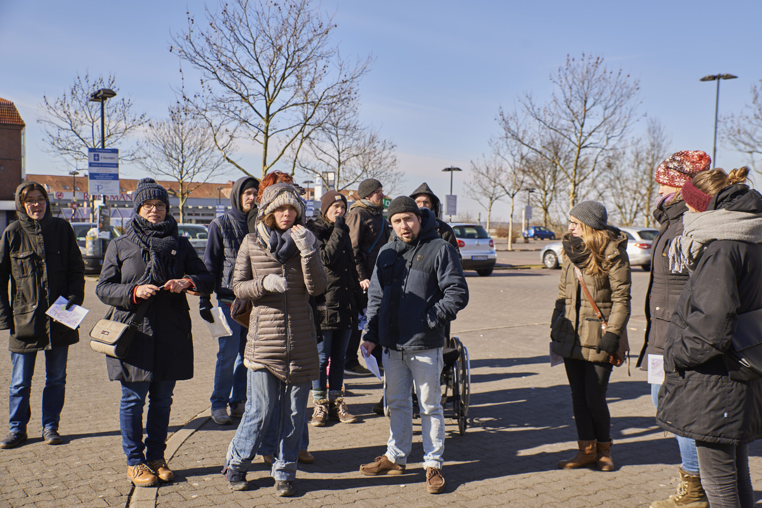 Eine Gruppe von etwa 20 Personen steht auf einem Parkplatz und diskutiert bei Kälte.