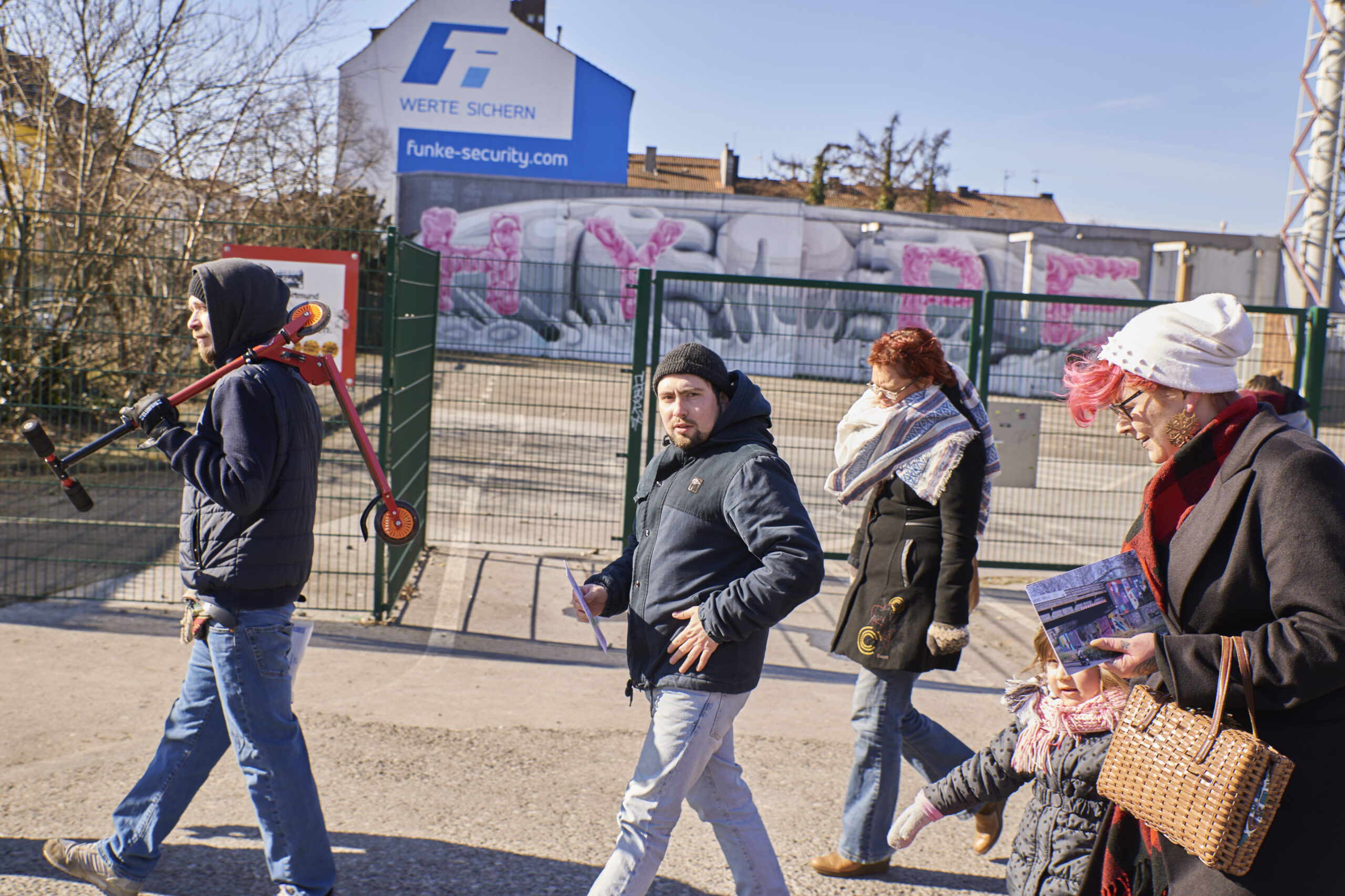 Eine Gruppe von Menschen spaziert an einem graue Gebäude mit rosa Graffiti vorbei.