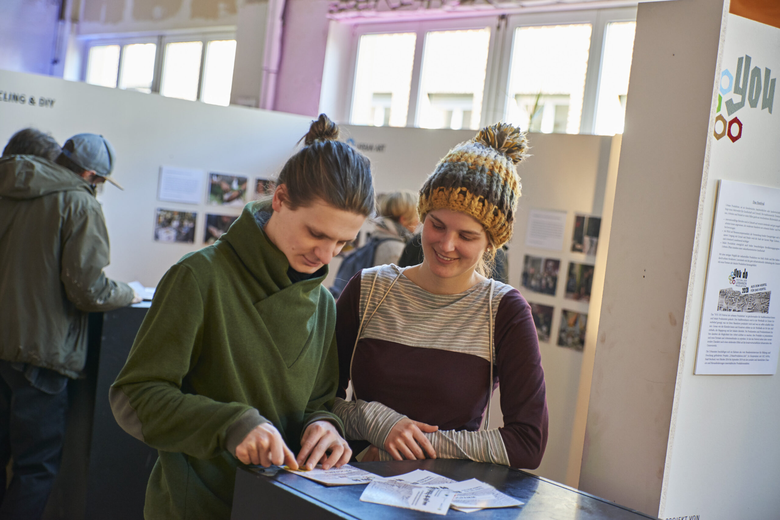 Zwei junge Frauen betrachten gemeinsam ein Dokument an einem Ausstellungstisch.