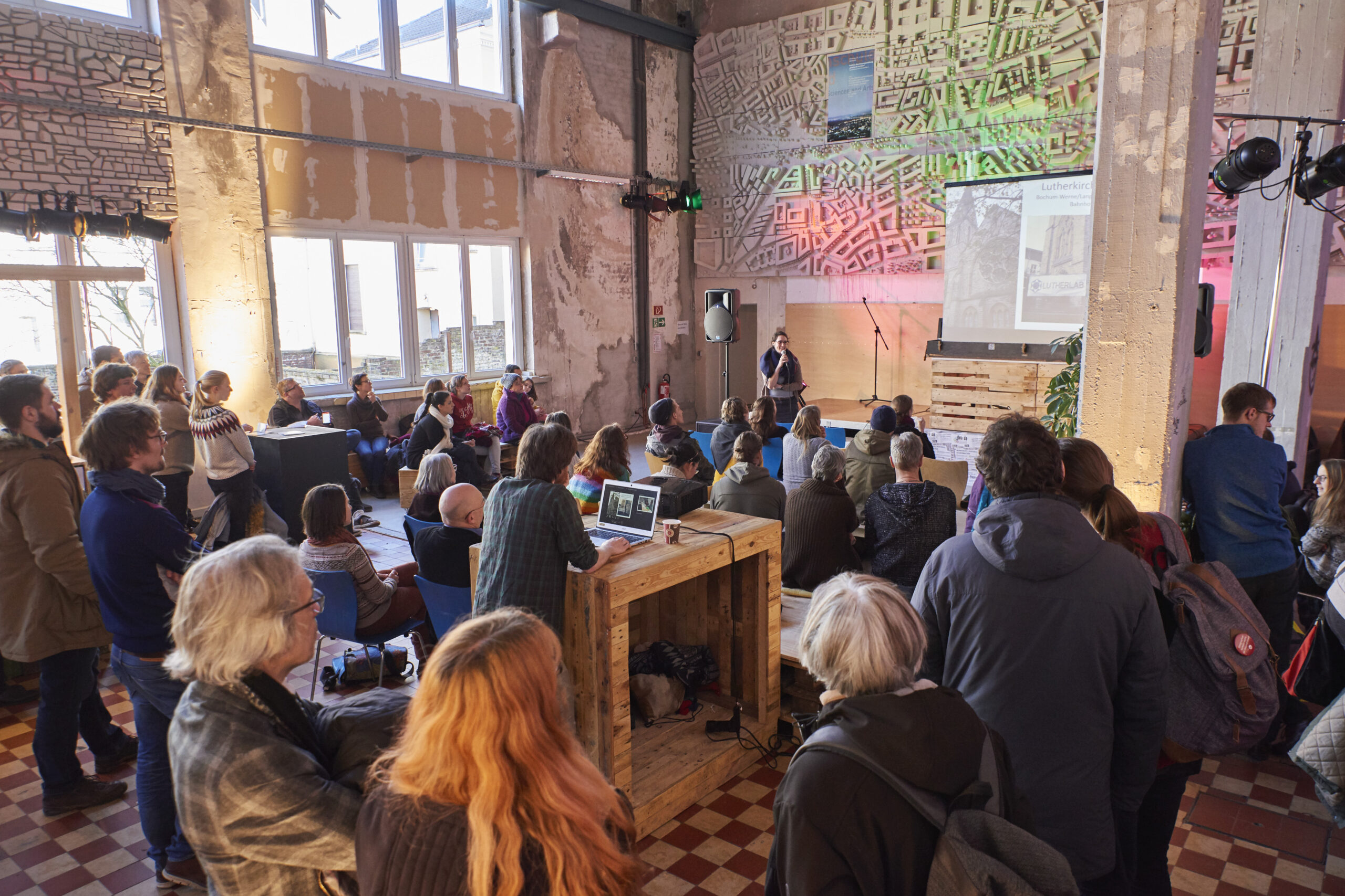 Etwa 50 Personen versammeln sich in einem Industrieloft zu einer Veranstaltung über Stadtentwicklung.