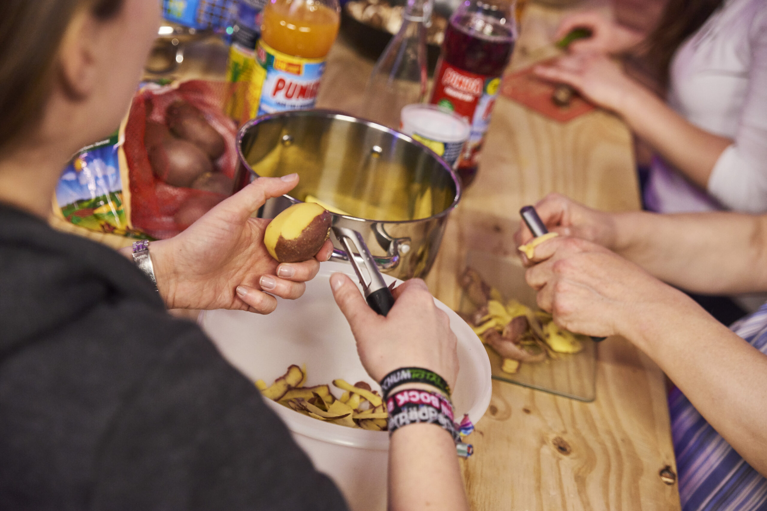 Mehrere Personen schneiden gemeinsam Kartoffeln an einem Holztisch zu.