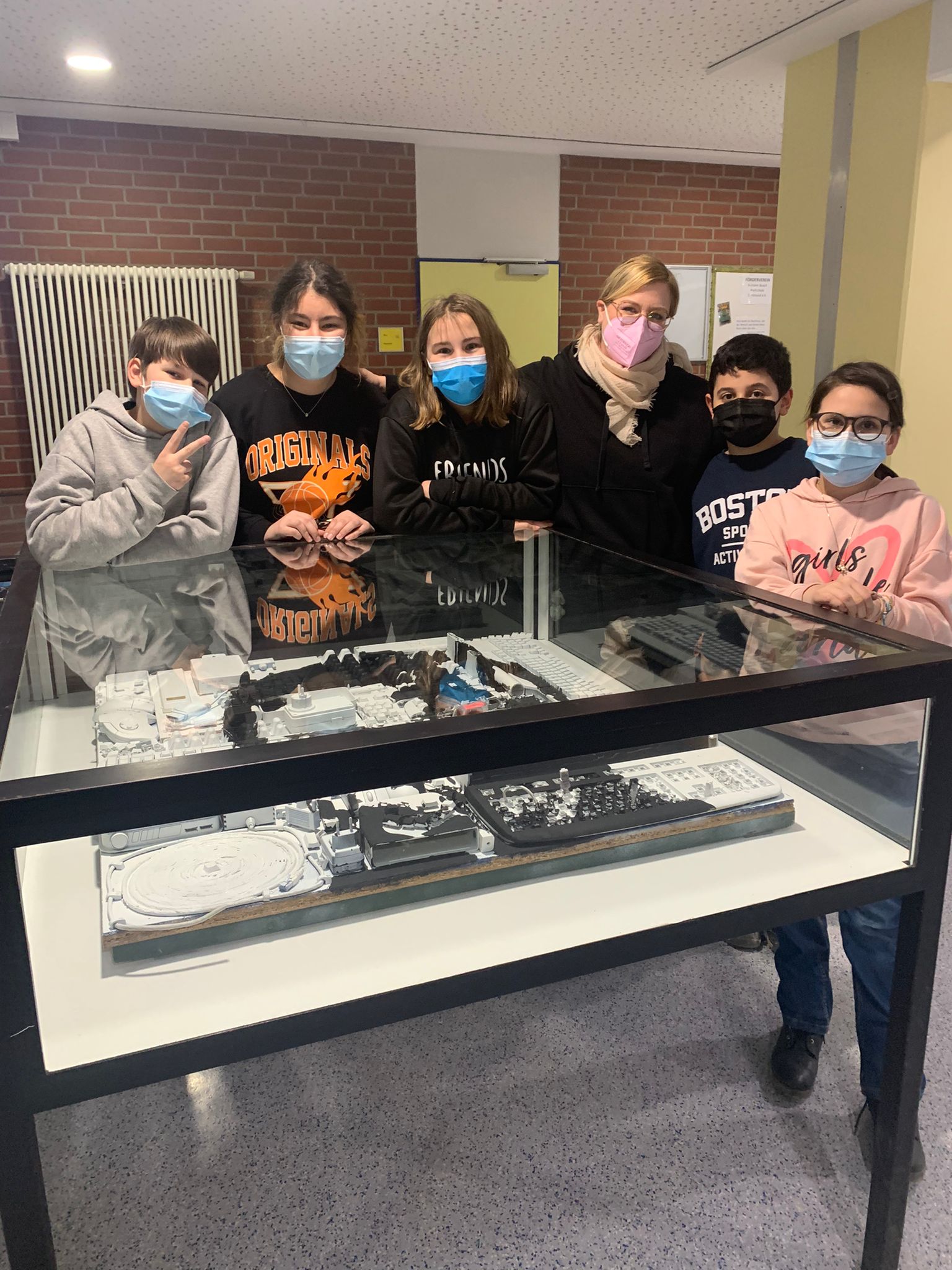 Sechs junge Menschen stehen an einer Ausstellungsvitrine mit technischen Geräten und Komponenten.