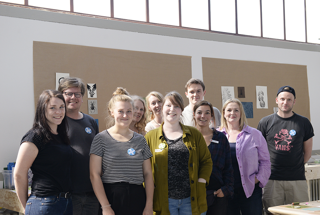 Gruppe von etwa zwölf Personen steht lächelnd vor einer Wand mit Kunstwerken in einem Innenraum.