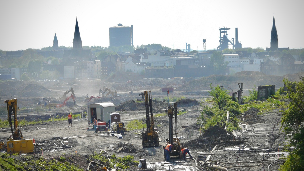 Baustelle im Vordergrund mit Baggern, dahinter Dortmunder Skyline mit Kirchen und Industriegebäuden.
