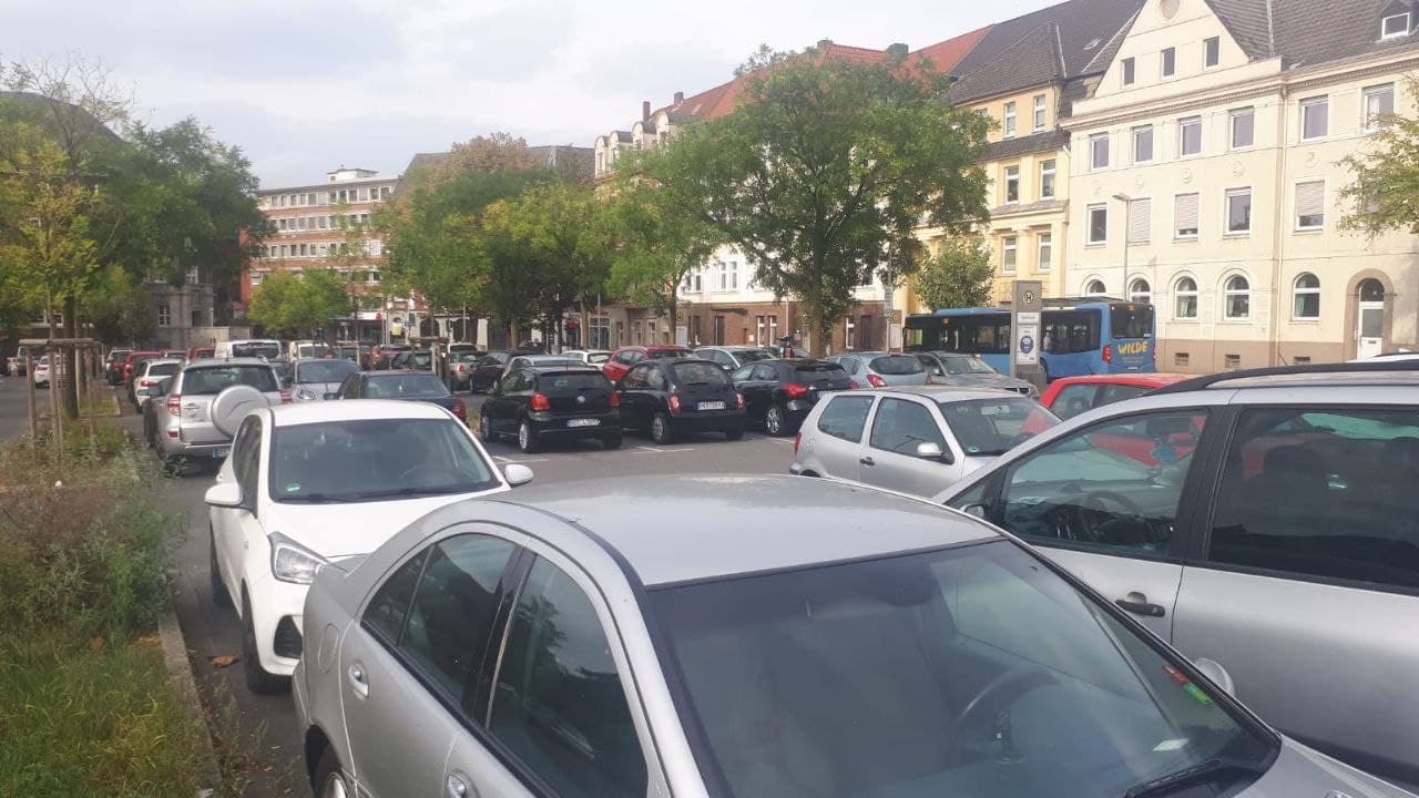 Vollgepackter Parkplatz mit zahlreichen Autos vor mehrstöckigen Wohngebäuden in urbaner Umgebung.