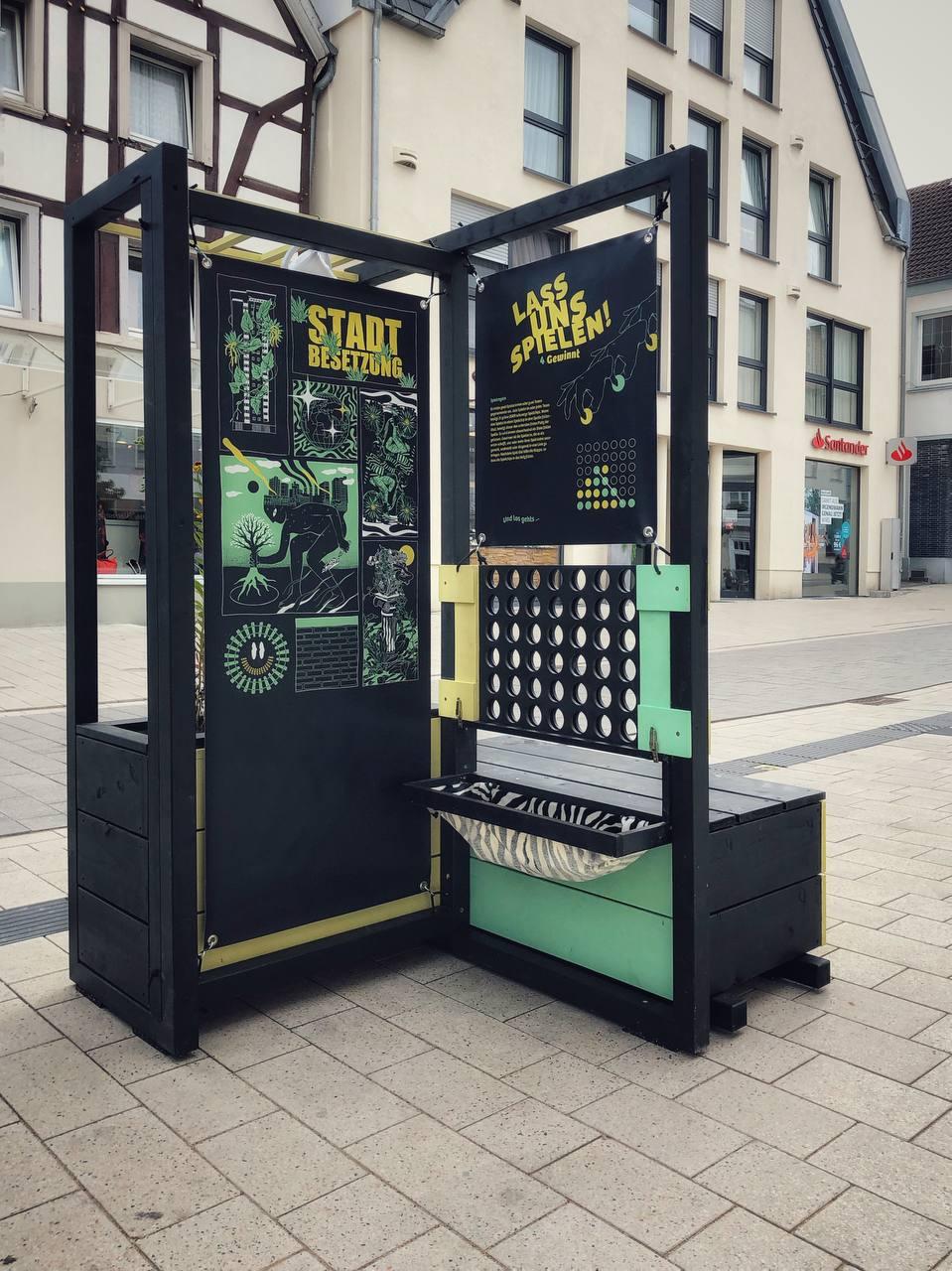 Schwarze Infokiosk-Box mit grünen Elementen und Grafiken zur Stadtbegrünung auf Dortmunder Platz.