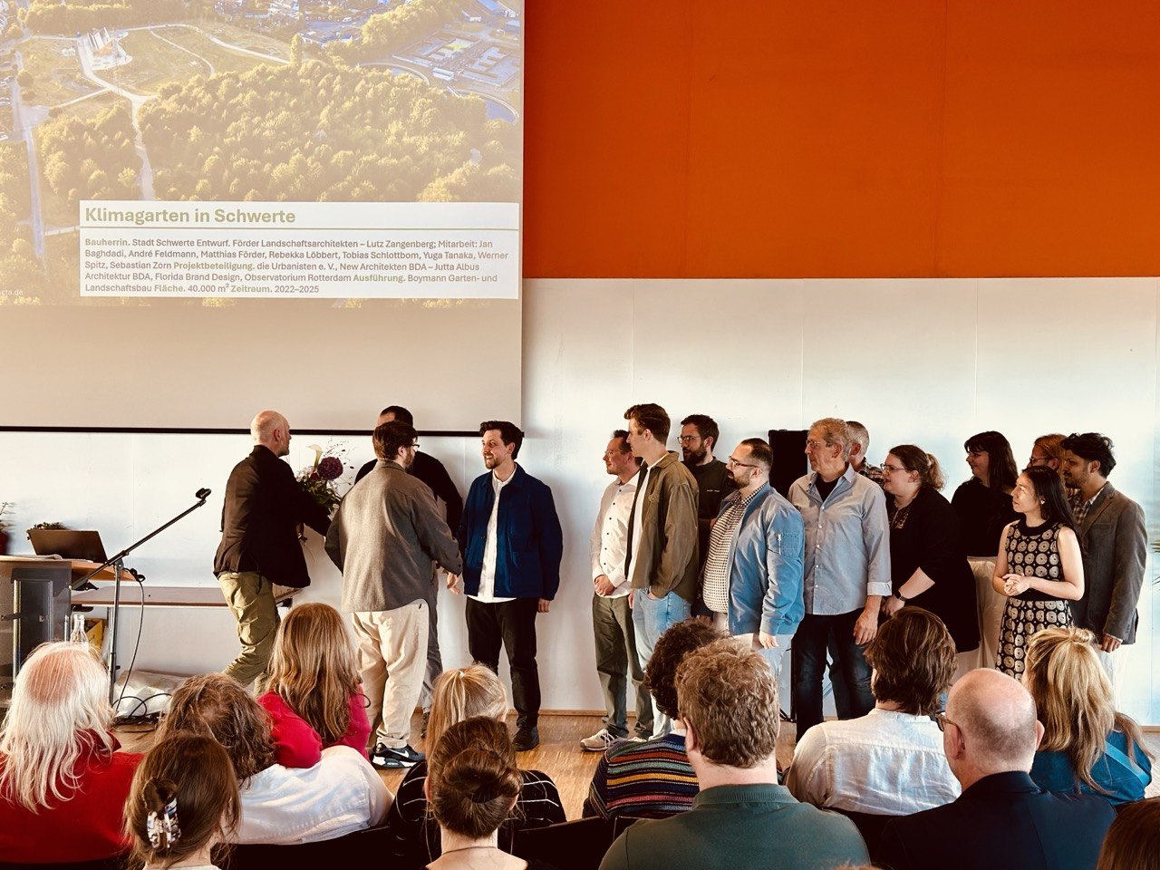 Etwa zwölf Personen stehen vor einer Leinwand mit Luftaufnahme des Klimagartens Schwerte und nehmen einen Preis entgegen.
