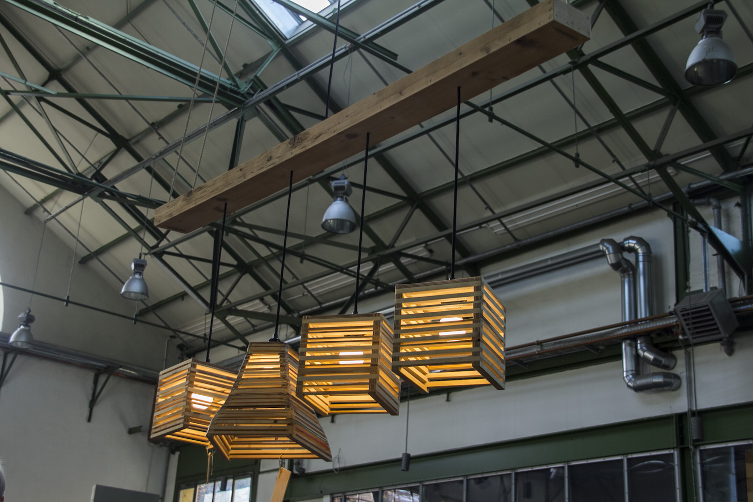 Industrielle Hallendecke mit hängenden Holzkisten-Leuchten und metallischen Bauelementen.
