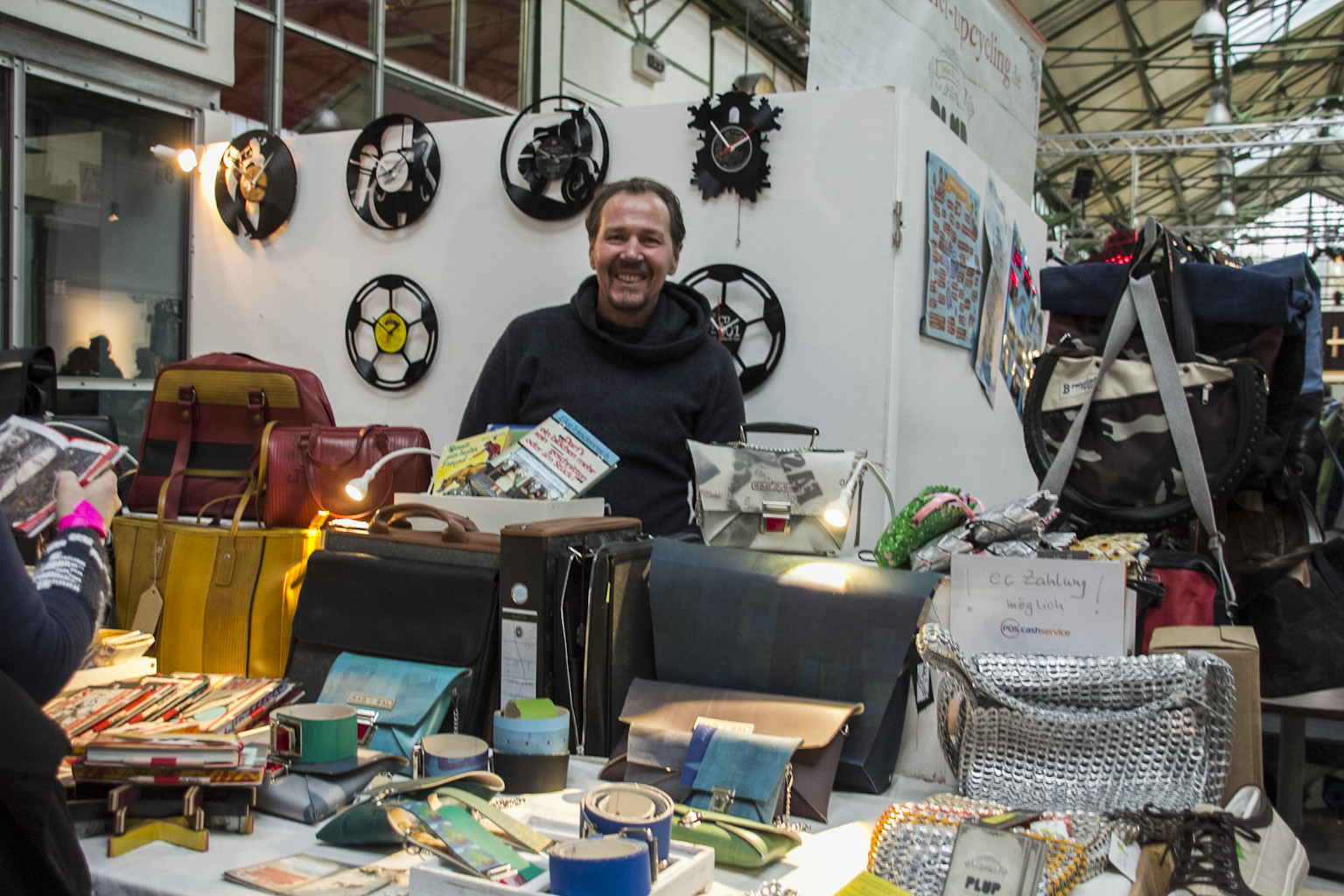 Ein Mann präsentiert an einem Stand handgefertigte Taschen und Accessoires aus Upcycling-Materialien.