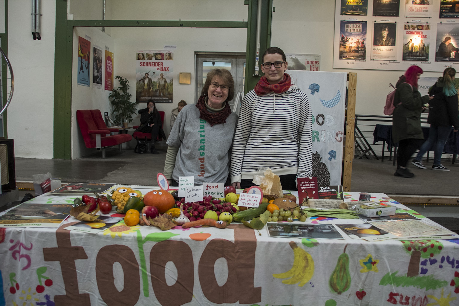 Zwei Personen präsentieren an einem Markttisch mit Obst und Gemüse ein Nachhaltigkeitsprojekt.