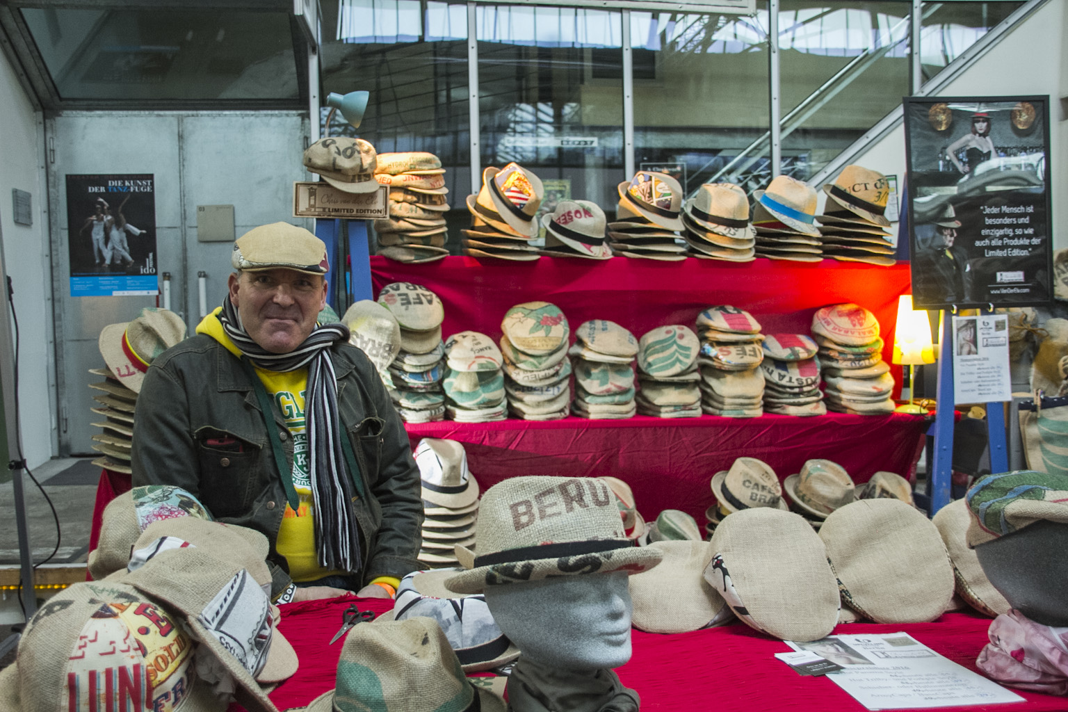 Ein Mann präsentiert an einem Stand eine umfangreiche Sammlung von Strohhüten verschiedener Stile und Farben.