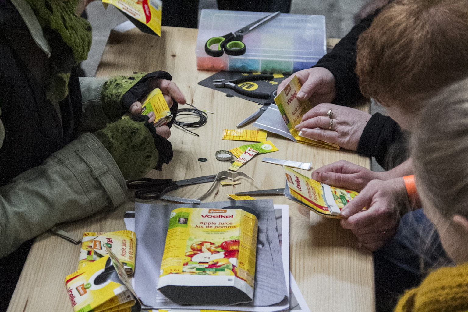Mehrere Personen untersuchen an einem Tisch Verpackungen von Lebensmitteln und Werkzeugen.