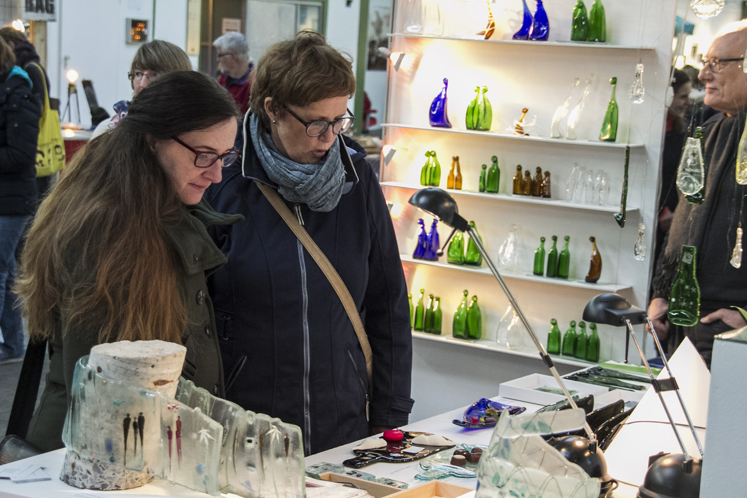 Zwei Personen betrachten Ausstellungsstücke an einem Tisch in einer Galerie mit beleuchteten Glasregalen.